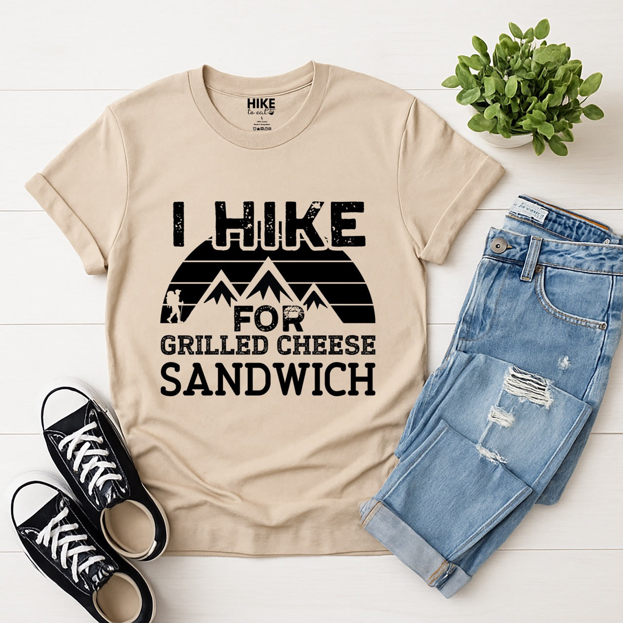 sand (beige)  I Hike for Grilled cheese Sandwich statement tee with bold distressed typography, geometric mountain design, and hiker silhouette for grilled cheese-loving outdoor enthusiasts, hikers and foodies laid flat with shoes and pants