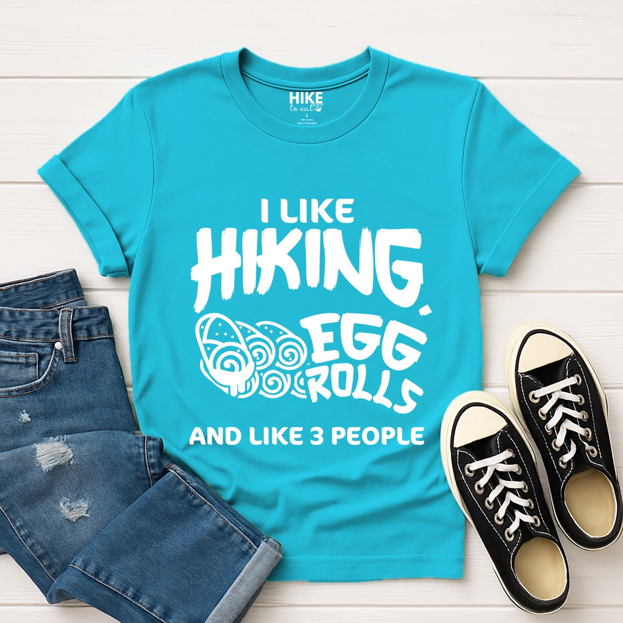 Tropical blue I like Hiking, Egg Rolls and like 3 People funny introvert statement tee with bold brushstroke typography and egg roll illustrations for Asian food-loving outdoor enthusiasts, hikers and foodies laid flat with shoes and pants
