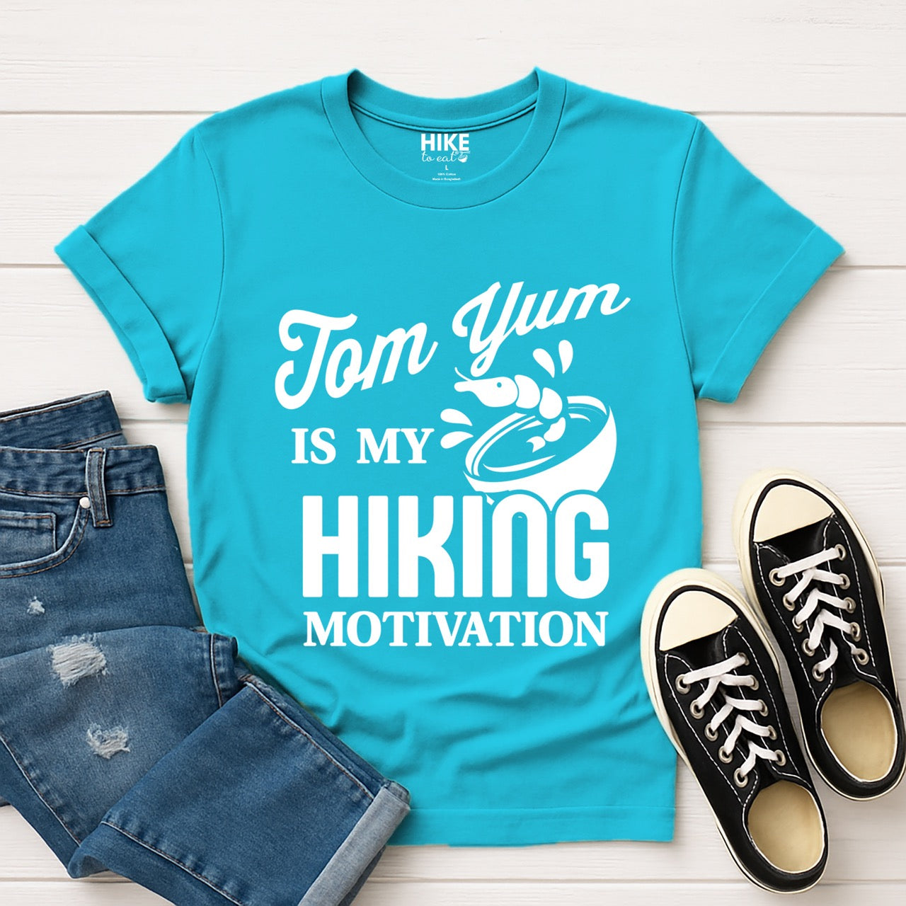 Tropical blue Tom Yum is my Hiking Motivation statement tee with flowing script and bold typography, shrimp and soup bowl illustration for Thai food-loving outdoor enthusiasts, hikers and foodies with shoes and pants