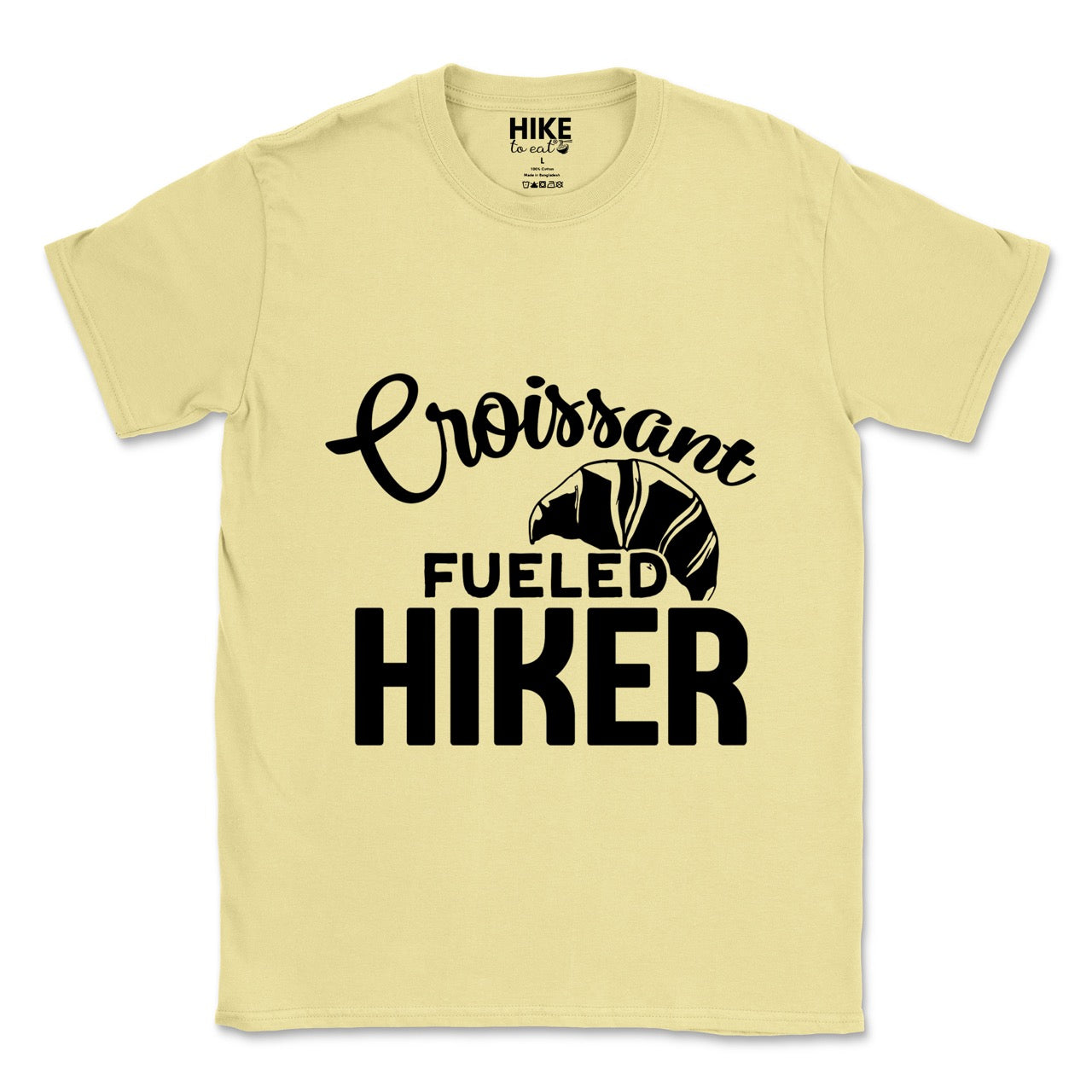 Cornsilk (yellow) Croissant Fueled Hiker statement tee with flowing script typography, bold lettering, and croissant illustration for French pastry-loving outdoor enthusiasts, hikers and foodies