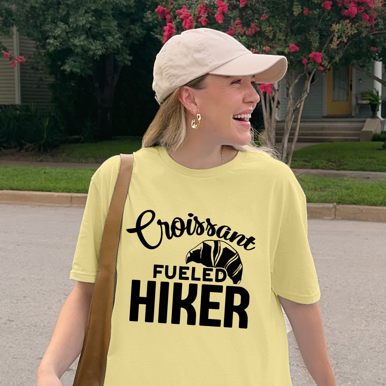 Woman wearing Cornsilk (yellow) Croissant Fueled Hiker statement tee with flowing script typography, bold lettering, and croissant illustration for French pastry-loving outdoor enthusiasts, hikers and foodies