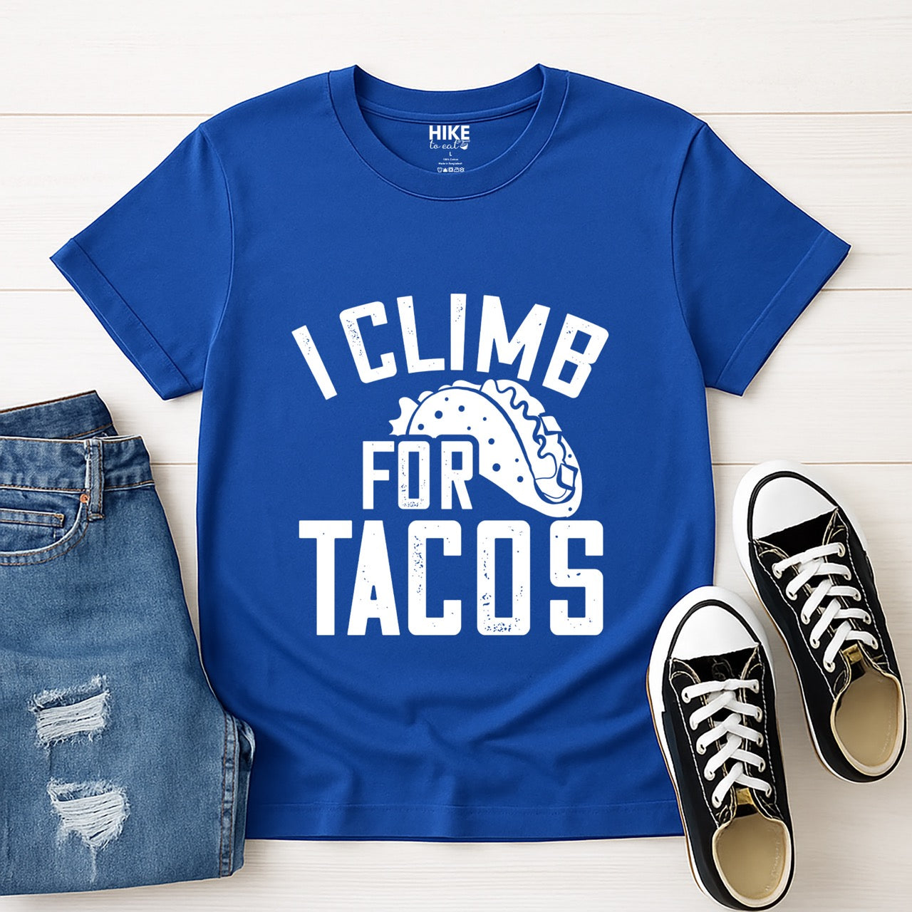 Royal I climb for Tacos statement tee with bold distressed curved typography and detailed taco illustration for Mexican food-loving rock climbers and nature hikers laid flat with pants and shoes