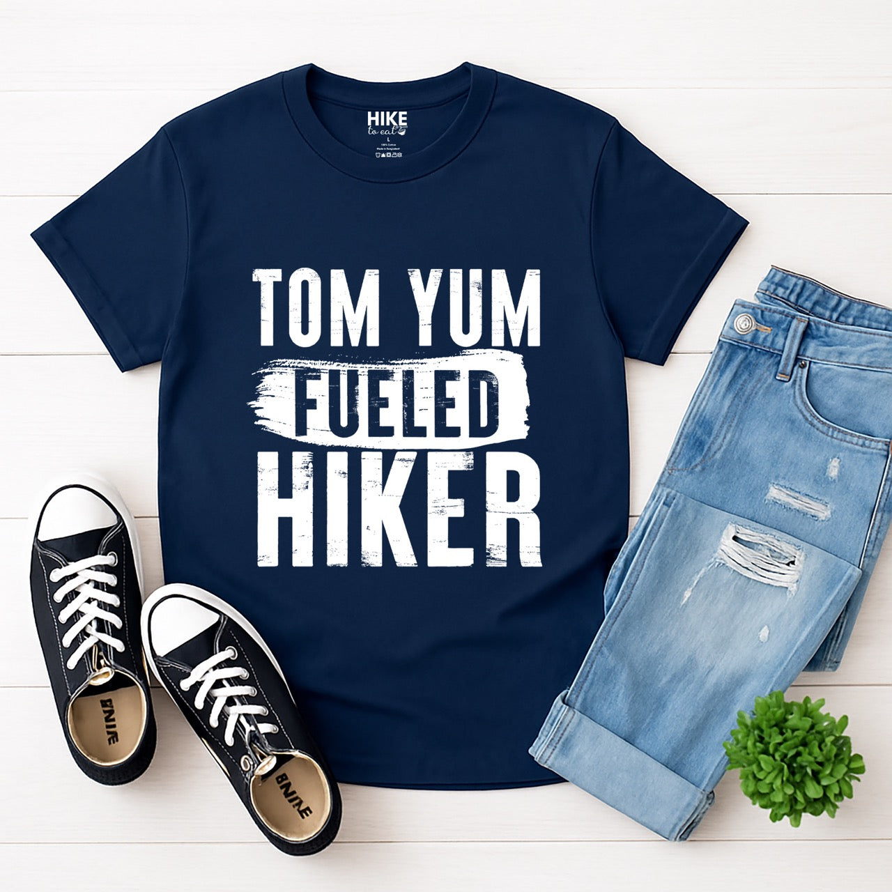 Navy Tom Yum Fueled Hiker statement tee with bold distressed typography and brushstroke design for Thai soup-loving outdoor enthusiasts, hikers and foodies laid flat with shoes and pants