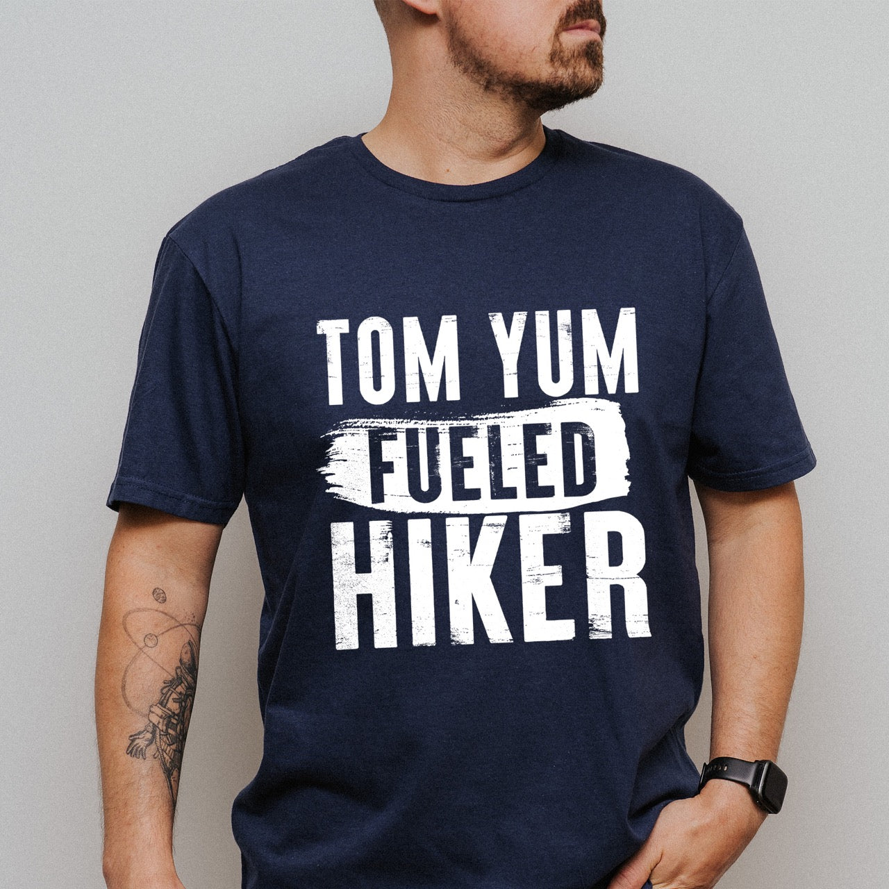 Man wearing Navy Tom Yum Fueled Hiker statement tee with bold distressed typography and brushstroke design for Thai soup-loving outdoor enthusiasts, hikers and foodies
