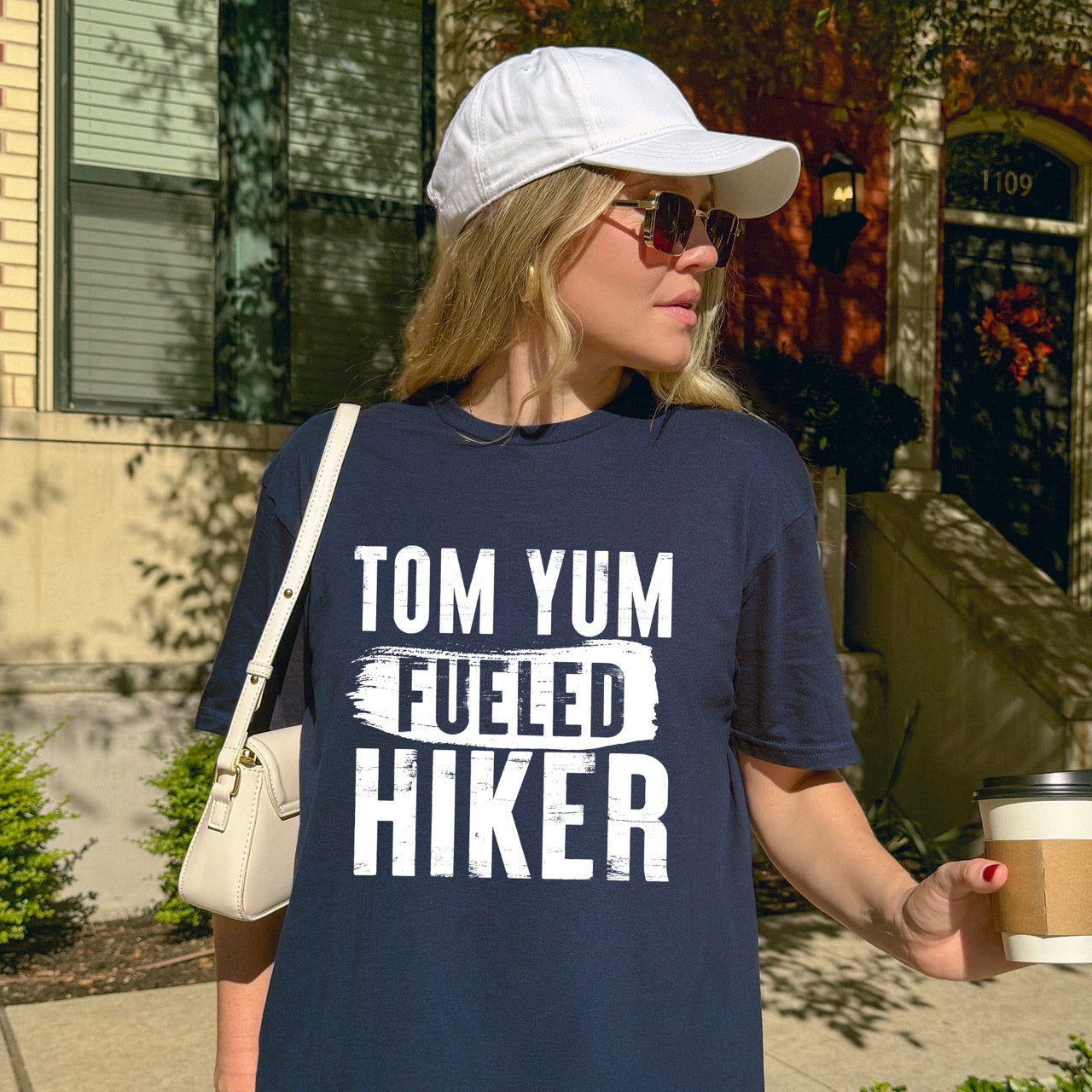 Woman wearing Navy Tom Yum Fueled Hiker statement tee with bold distressed typography and brushstroke design for Thai soup-loving outdoor enthusiasts, hikers and foodies
