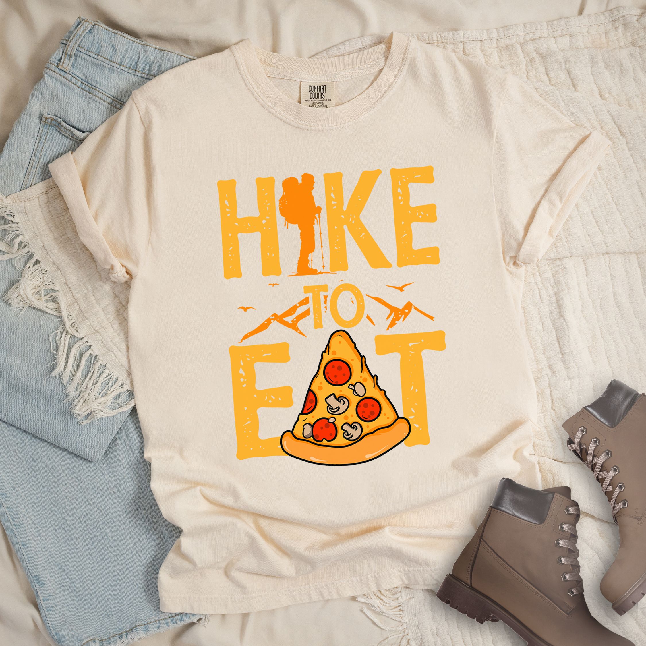 Ivory shirt with a Hiking design of a slice of pizza and shows 'Hike To Eat' phrase in bold text