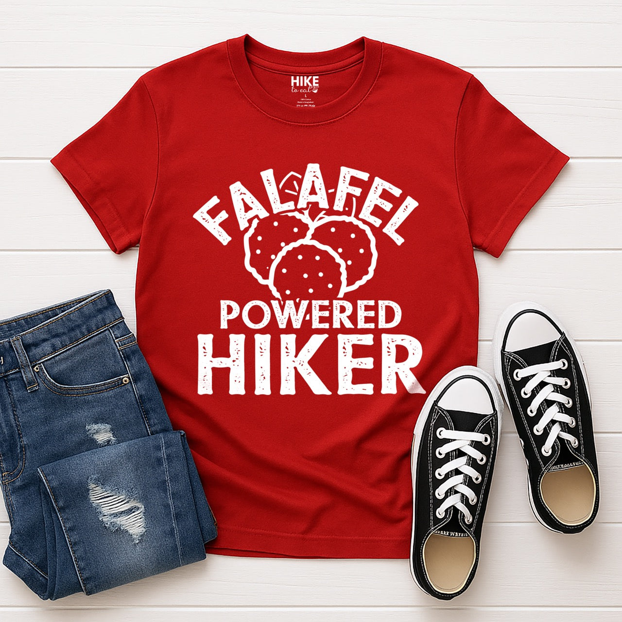 Red Falafel Powered Hiker statement tee with bold distressed curved typography and detailed falafel illustration for Middle Eastern food-loving outdoor enthusiasts, foodies and hikers laid flat with shoes and pants