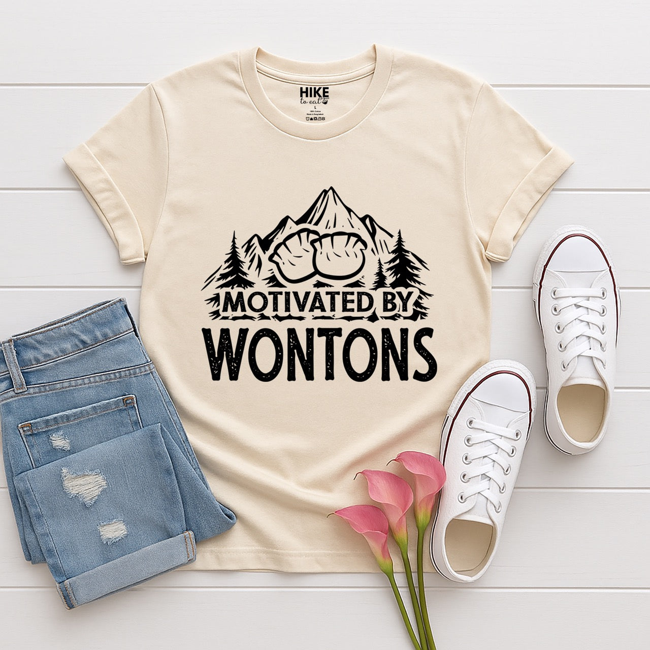 Natural (beige) Motivated by Wontons statement tee with bold distressed typography, mountain peaks, pine trees, and wonton illustration for Chinese food-loving outdoor enthusiasts, hikers and foodies laid flat with shoes and pants