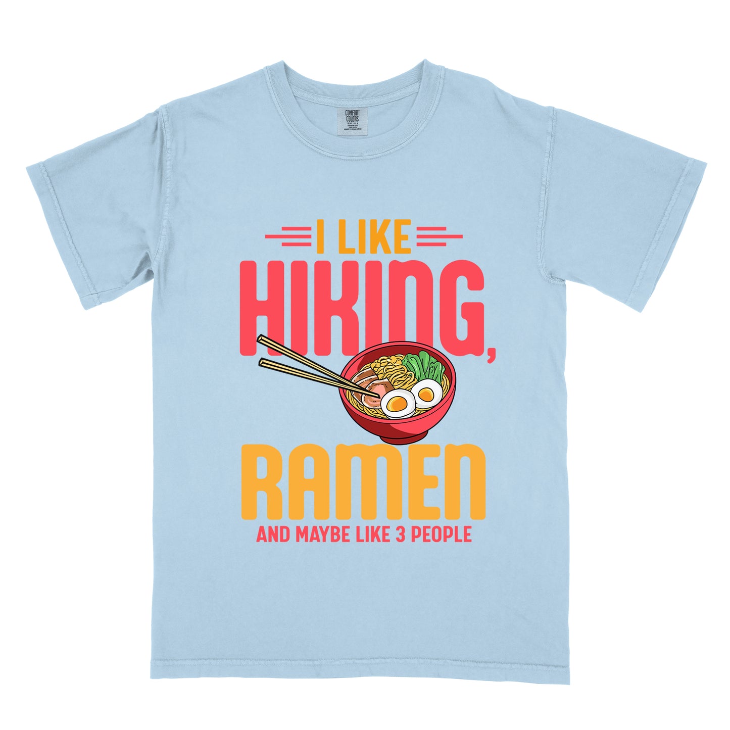 Chambray (Light Blue) t-shirt with text "I LIKE HIKING, RAMEN AND MAYBE LIKE 3 PEOPLE". "I LIKE" appears in orange at the top with red decorative lines, "HIKING," in large red letters, "RAMEN" in yellow/orange, and "AND MAYBE LIKE 3 PEOPLE" in red at the bottom. Between "HIKING" and "RAMEN" is a colorful illustration of a red ramen bowl with noodles, egg, and vegetables, with chopsticks.