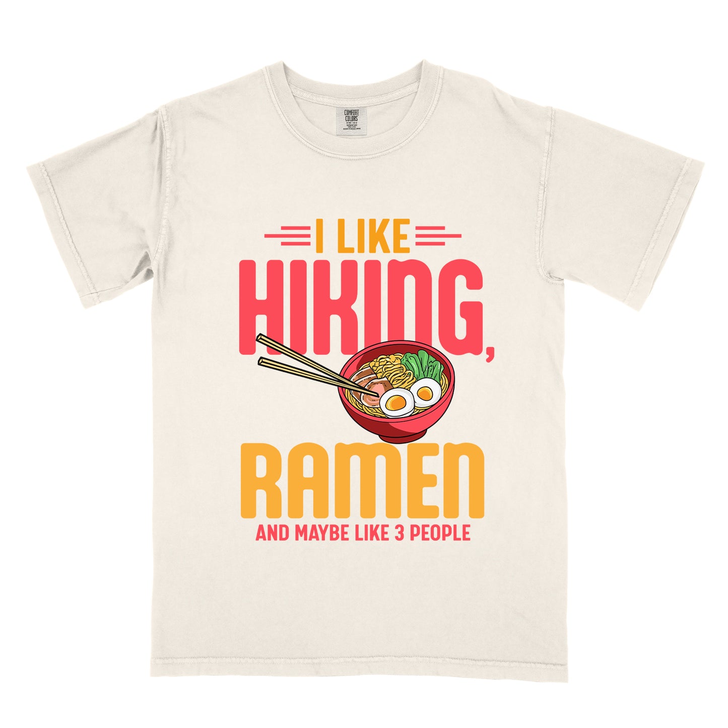 Ivory (Cream White) t-shirt with text "I LIKE HIKING, RAMEN AND MAYBE LIKE 3 PEOPLE". "I LIKE" appears in orange at the top with red decorative lines, "HIKING," in large red letters, "RAMEN" in yellow/orange, and "AND MAYBE LIKE 3 PEOPLE" in red at the bottom. Between "HIKING" and "RAMEN" is a colorful illustration of a red ramen bowl with noodles, egg, and vegetables, with chopsticks.