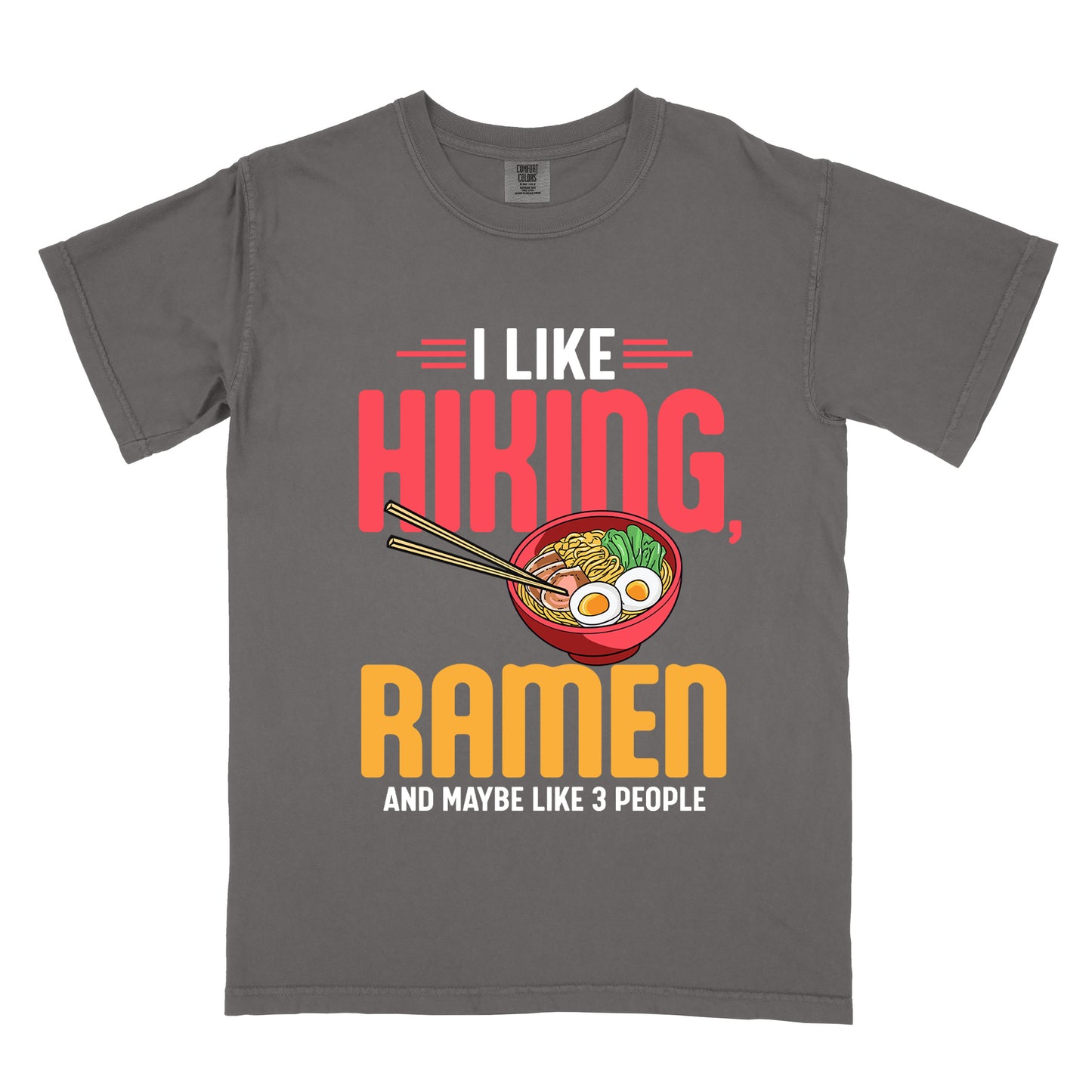 Pepper (Dark Gray) t-shirt with text "I LIKE HIKING, RAMEN AND MAYBE LIKE 3 PEOPLE". "I LIKE" appears in white at the top with red decorative lines, "HIKING," in large red letters, "RAMEN" in yellow/orange, and "AND MAYBE LIKE 3 PEOPLE" in white at the bottom. Between "HIKING" and "RAMEN" is a colorful illustration of a red ramen bowl with noodles, egg, and vegetables, with chopsticks.