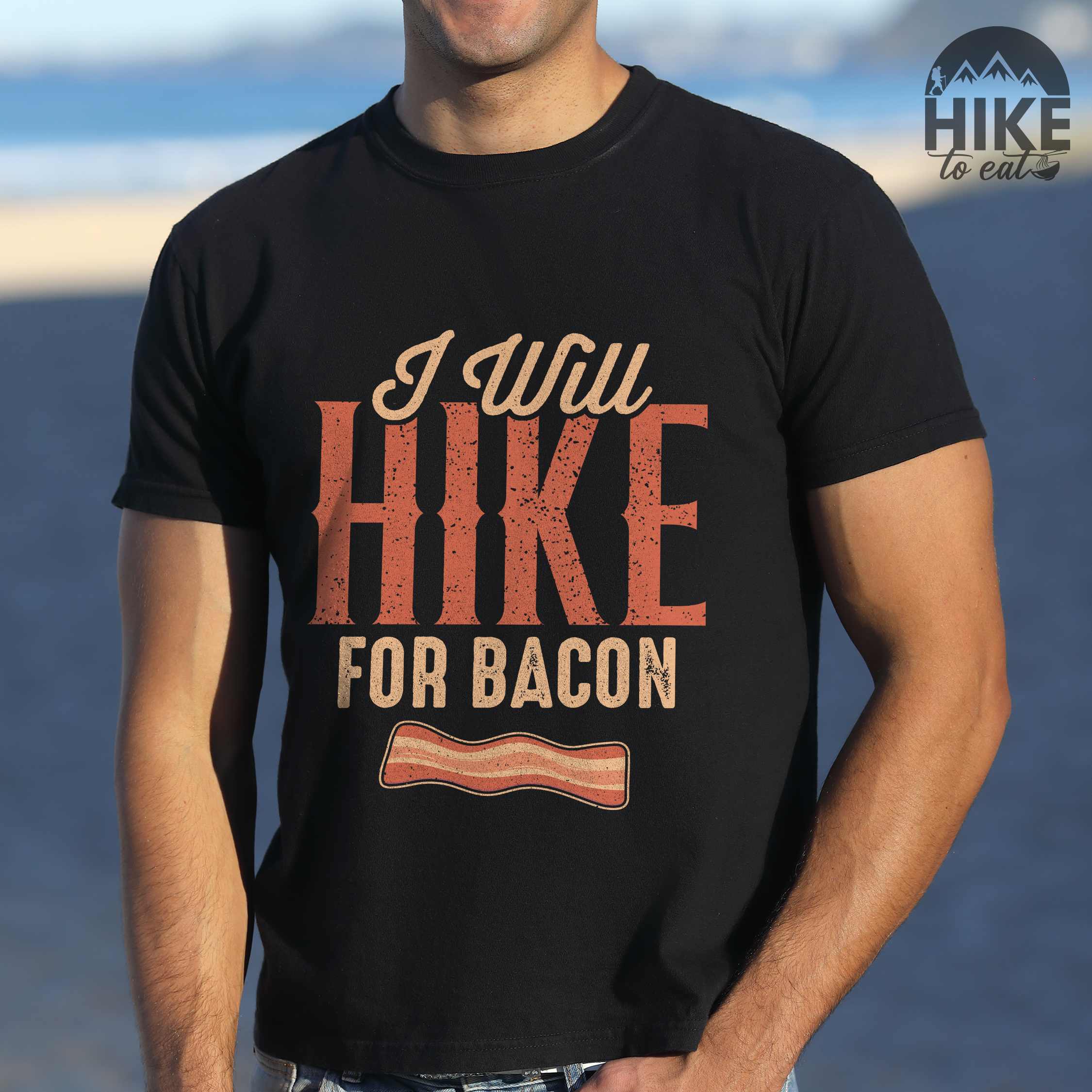 Man wearing black "I Will Hike for Bacon" colored vintage tee with bold typography, illustrated crispy bacon, perfect for breakfast lovers