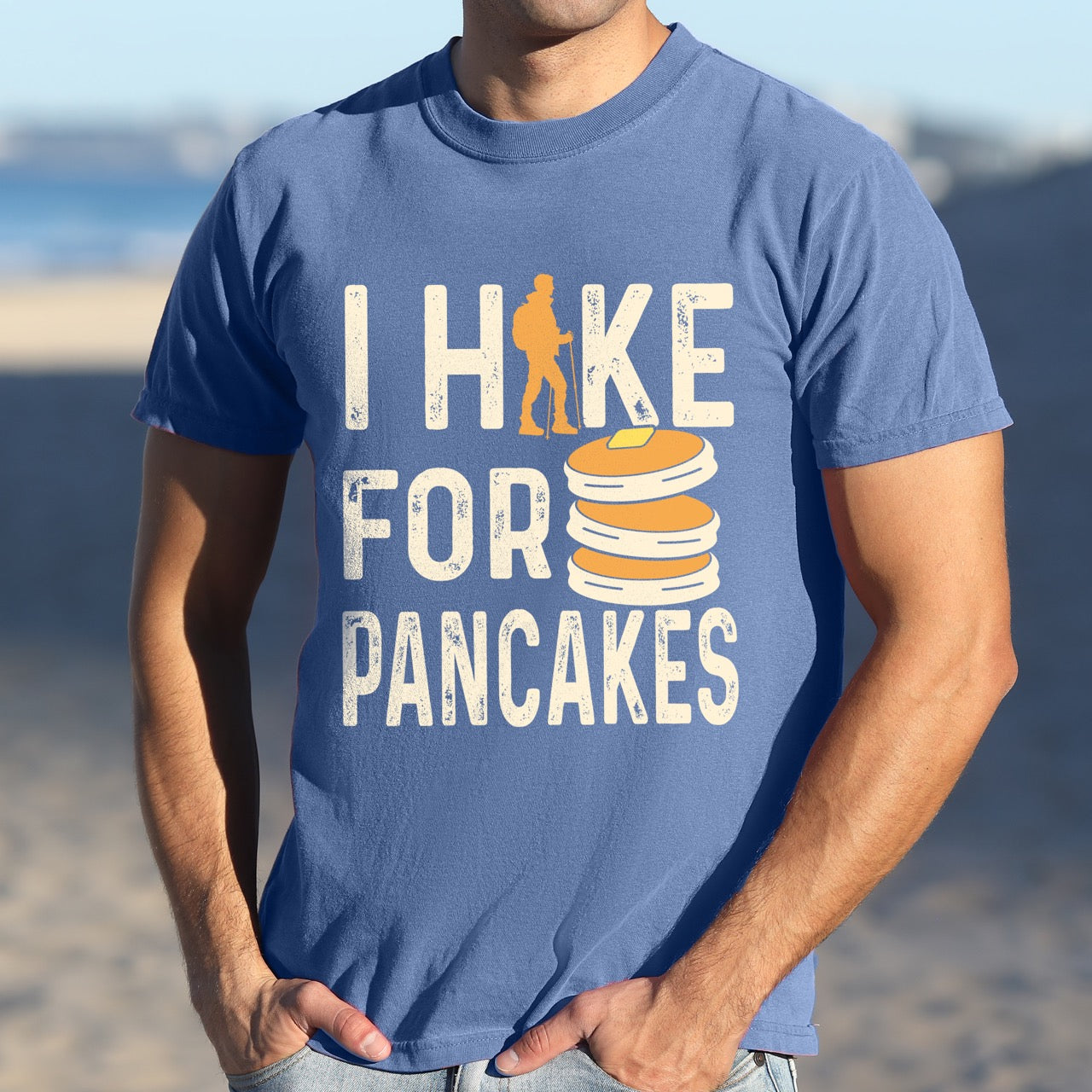 Man wearing blue jean colored Pancake breakfast lover vintage tee I Hike for Pancakes with distressed cream typography character silhouette with trekking pole and illustrated stacked pancakes with butter on Comfort Colors shirt for brunch and food enthusiasts, hikers and foodies.