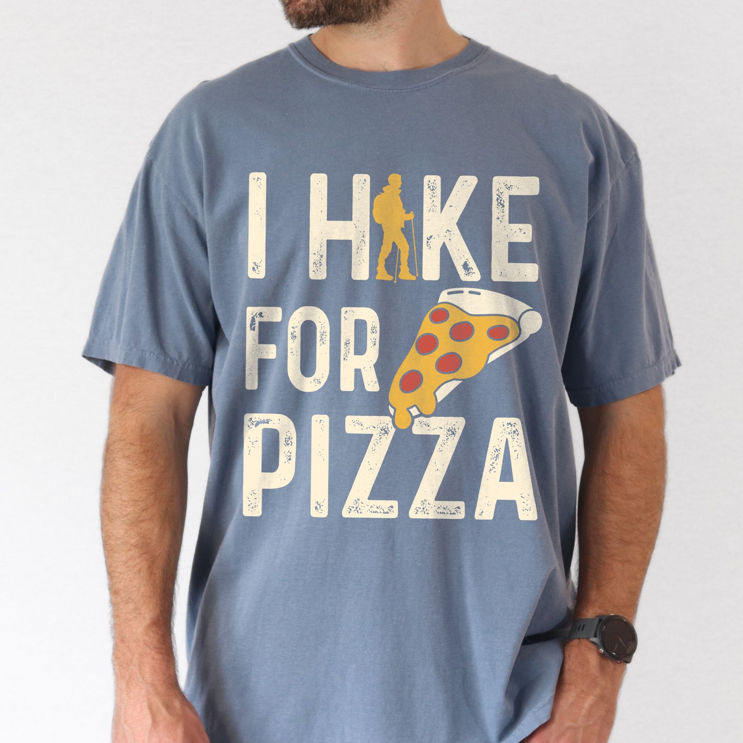 Blue Jean (Denim Blue) graphic t-shirt with 'I Hike for Pizza' text in cream lettering featuring orange hiker silhouette and pizza slice illustration with pepperoni toppings.