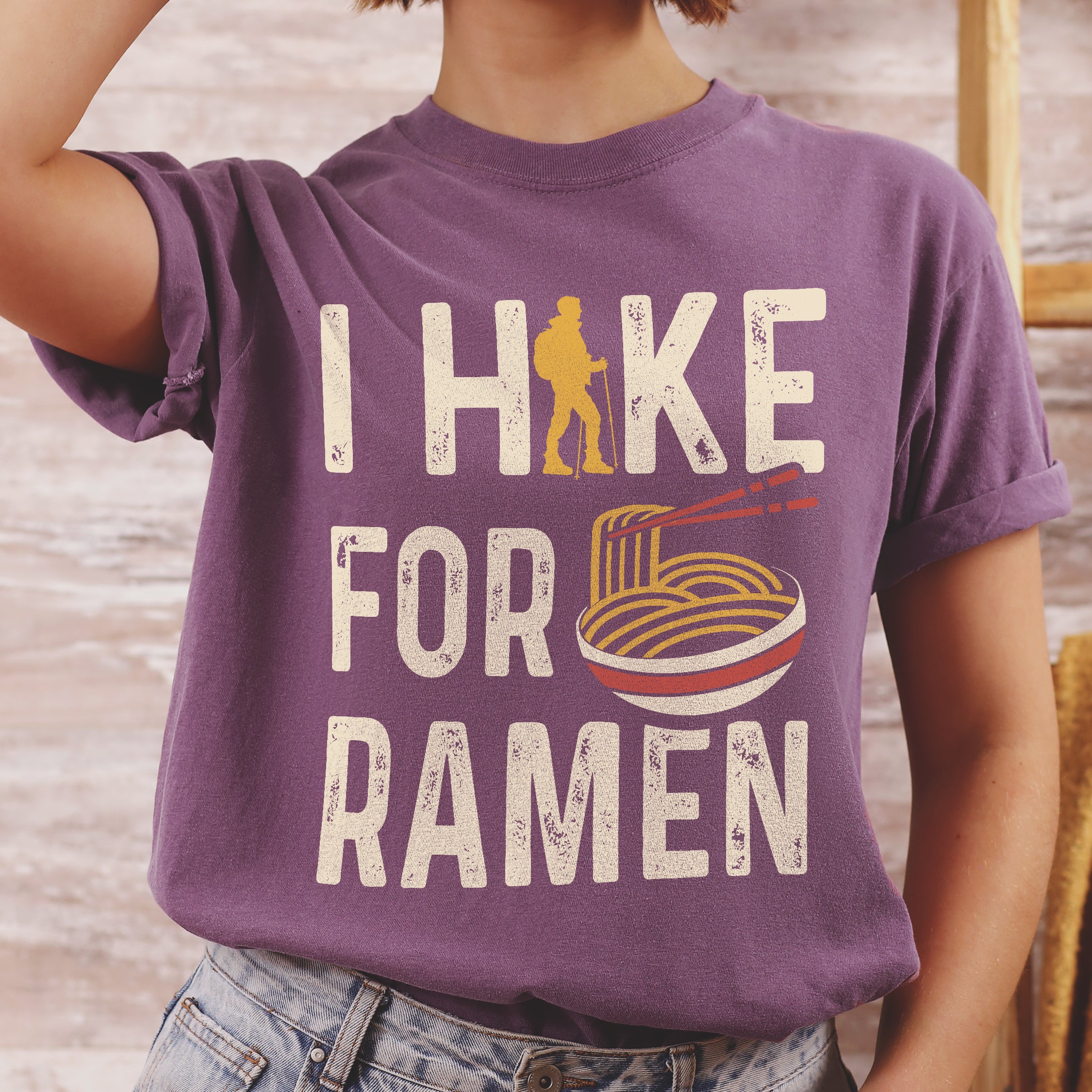 Berry (Dark Violet) graphic t-shirt with 'I Hike for Ramen' text in cream lettering featuring orange hiker silhouette and colorful ramen bowl illustration with noodles and chopsticks