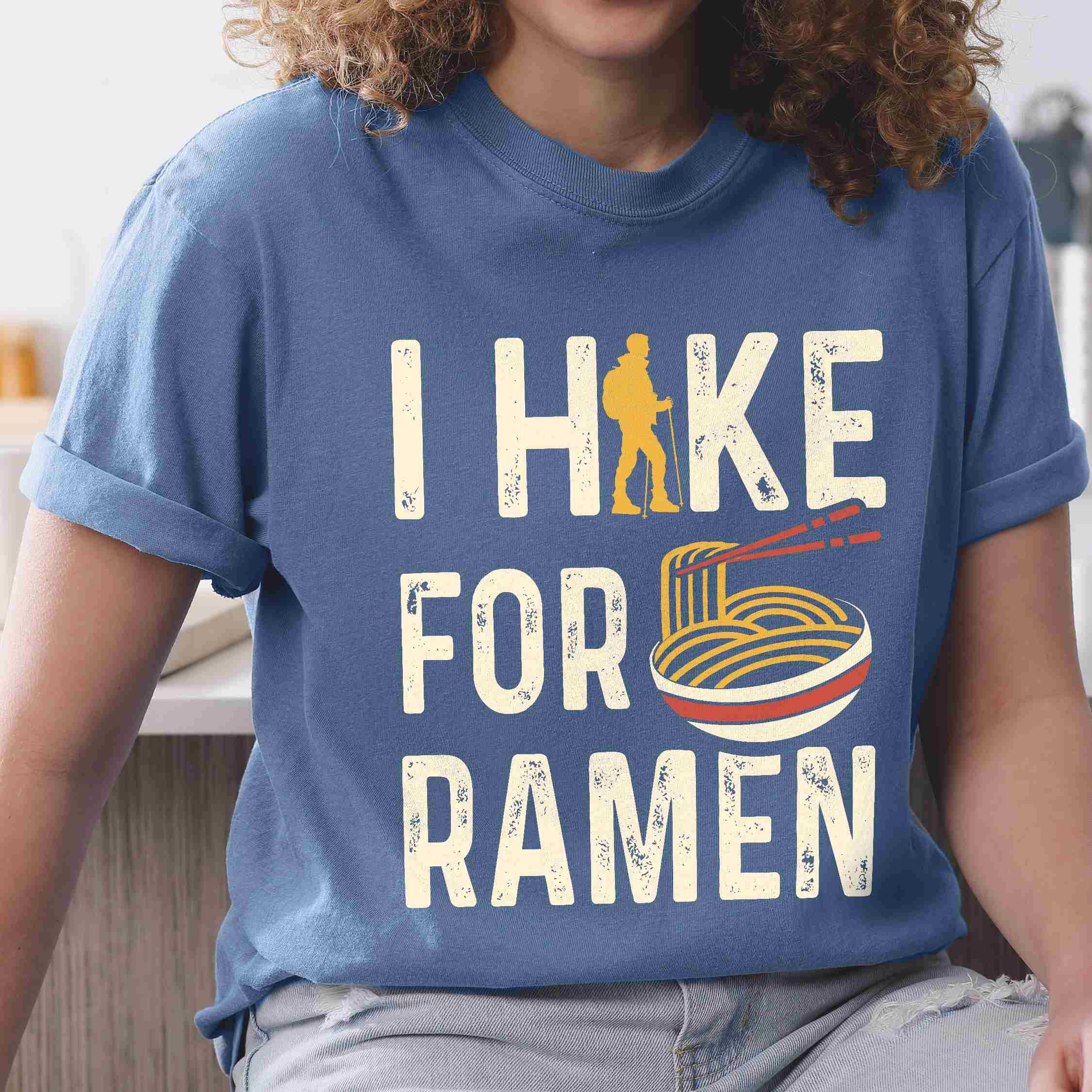 Woman wearing blue jean colored vintage tee with 'I Hike for Ramen' text in cream lettering, illustrated taco, and backpacker for ramen lovers