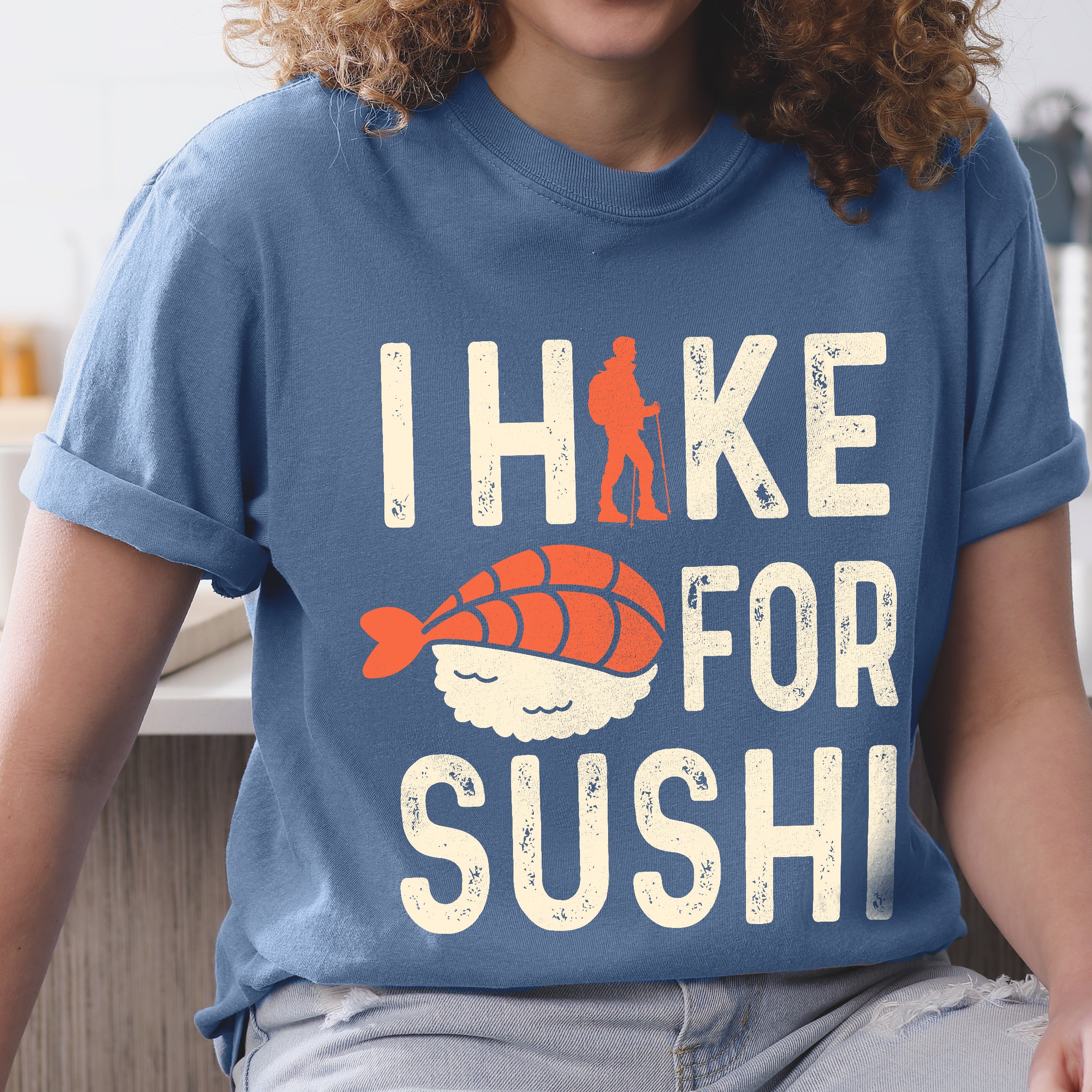 Blue Jean (Denim Blue) graphic t-shirt with 'I Hike for Sushi' text in cream lettering featuring orange hiker silhouette and sushi nigiri illustration with orange fish and white rice