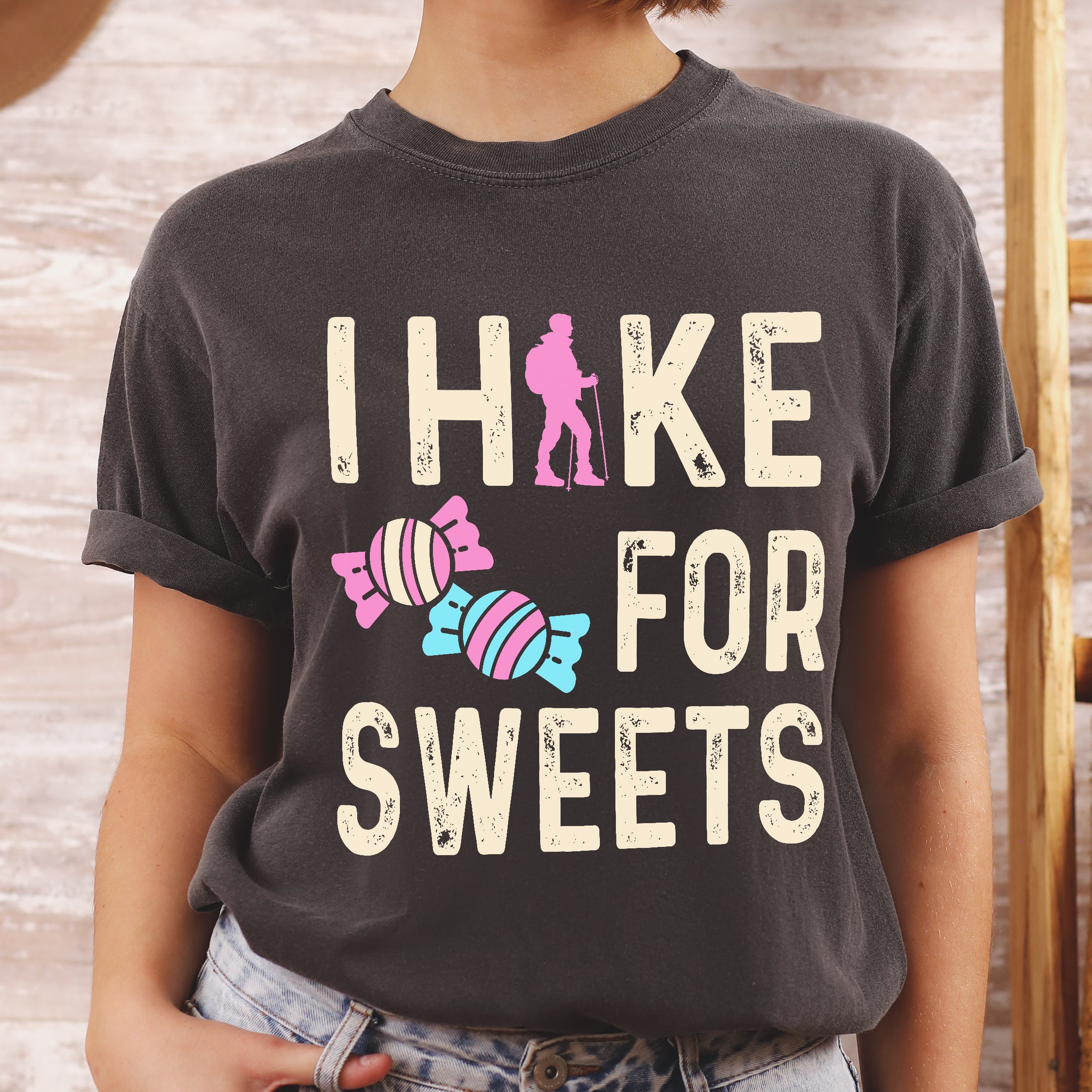 Pepper (Dark Gray) graphic t-shirt with 'I Hike for Sweets' text in cream lettering featuring pink hiker silhouette and colorful striped candy illustrations in pink and blue.