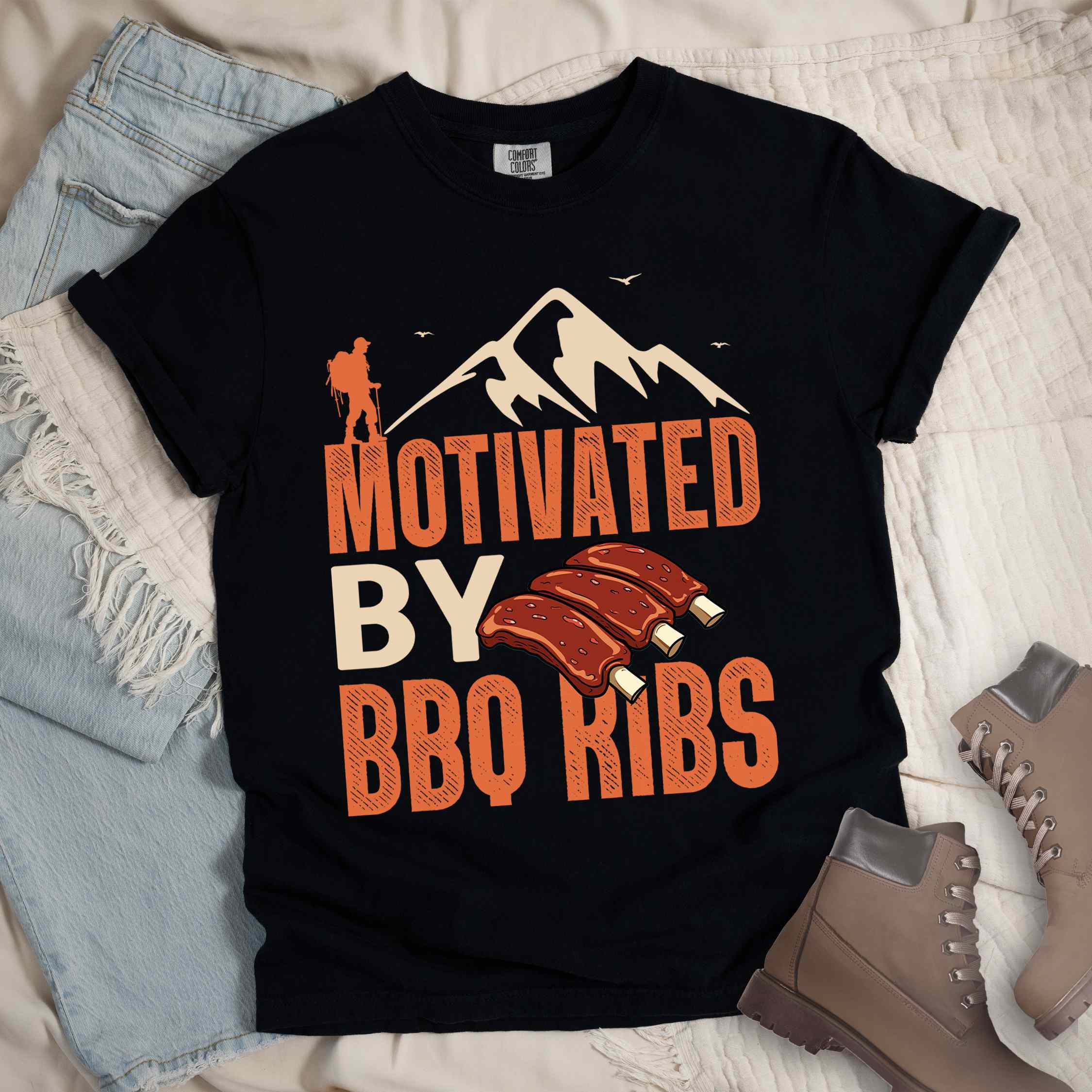 Black "Motivated by BBQ ribs" colored vintage tee with bold typography, mountains, juicy grilled bbq ribs illustration, and backpacker for bbq enthusiasts