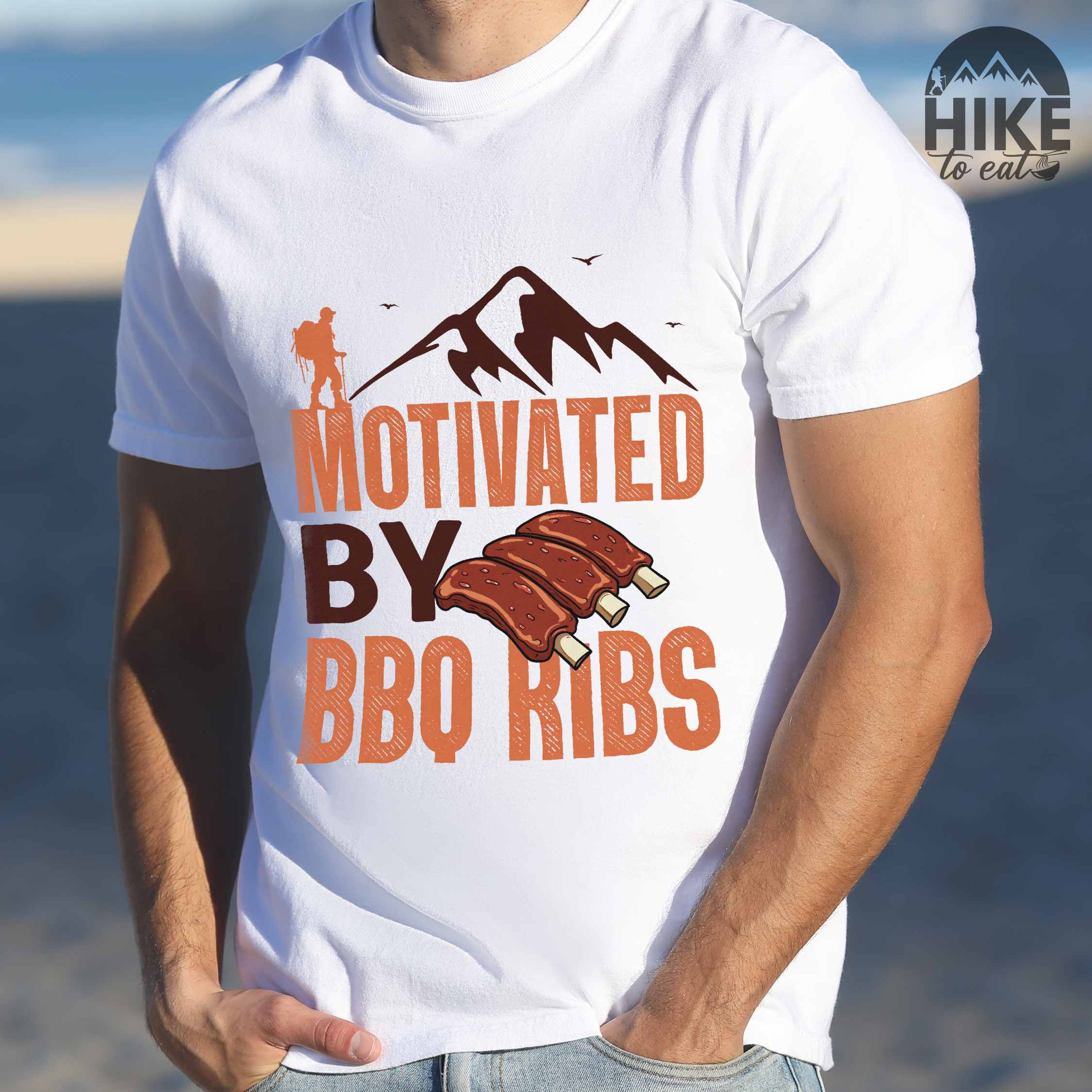 Man wearing white "Motivated by BBQ ribs" colored vintage tee with bold typography, mountains, juicy grilled bbq ribs illustration, and backpacker for bbq enthusiasts