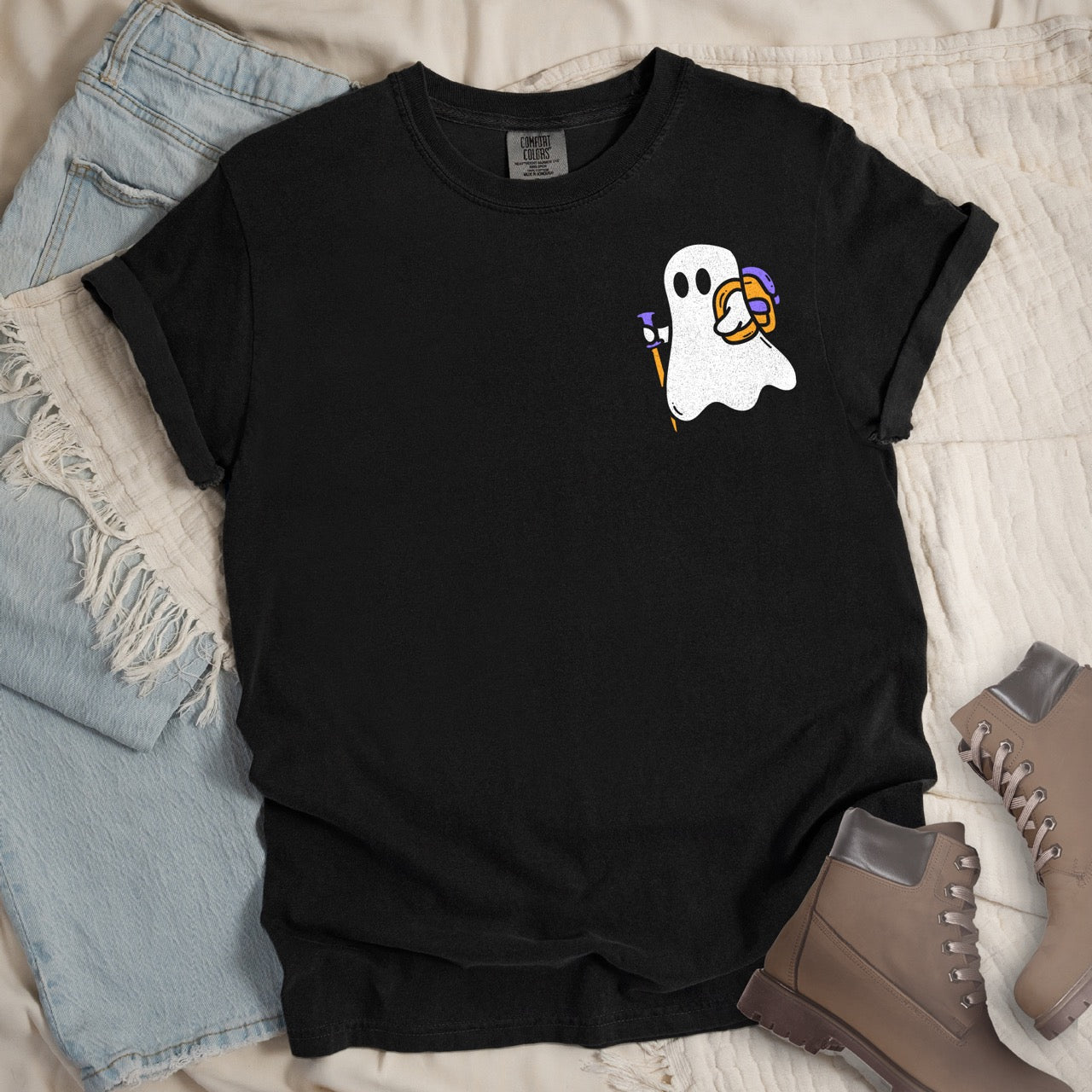  black Halloween ghost statement shirt featuring cute white Boo character with trekking pole and orange candy bucket filled with purple wrapped treats on chest placement Comfort Colors tee for spooky season celebrations for hikers and adventurers with pants and shoes.