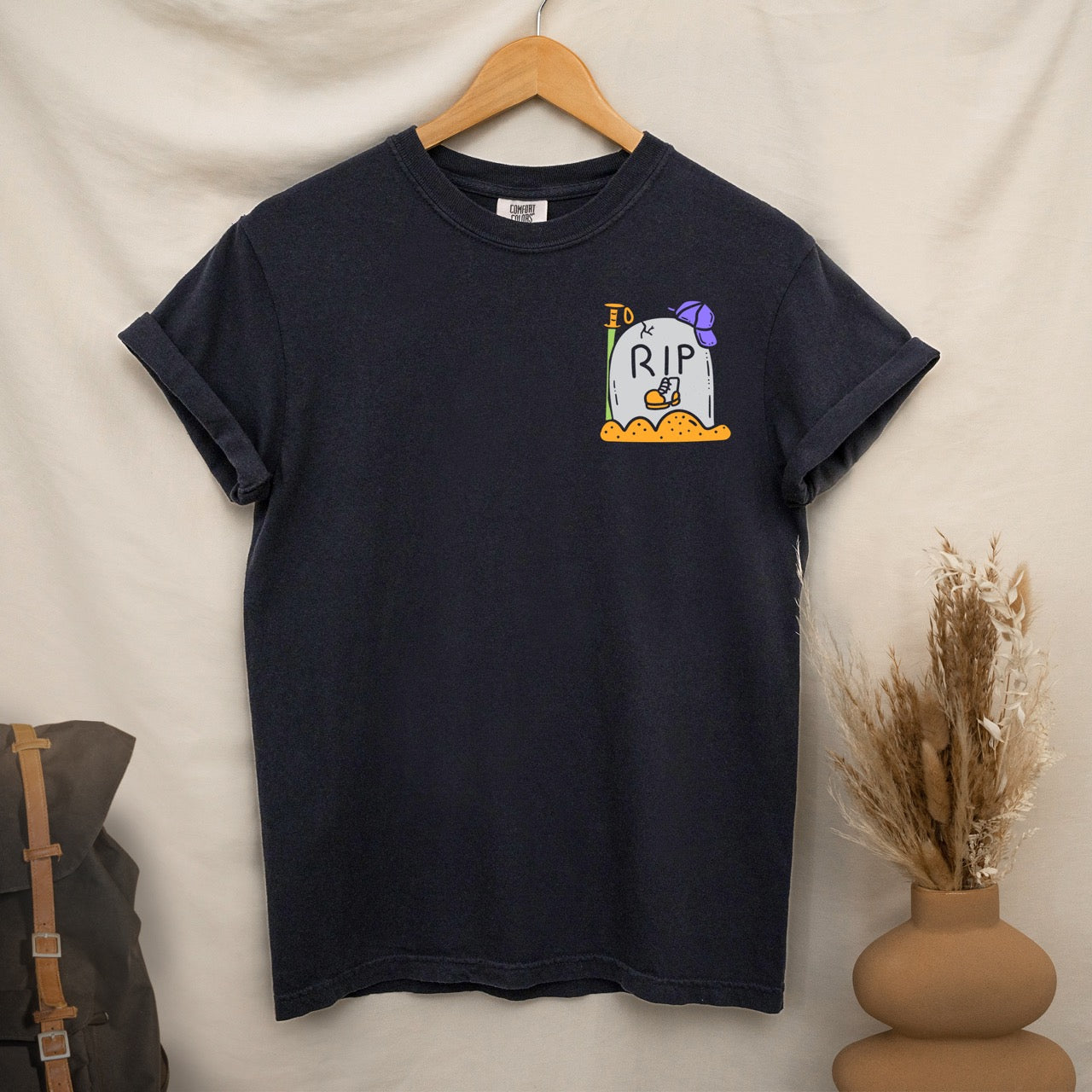 black t-shirt with a graphic design  of RIP boot on a hanger against a neutral background