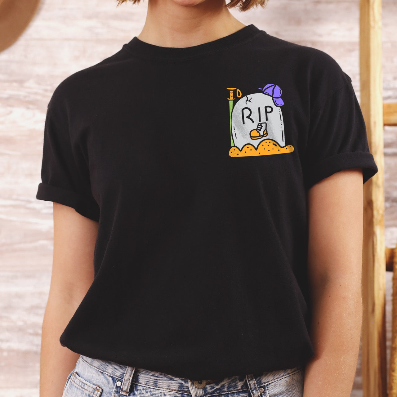 Person wearing a black t-shirt with a cartoon tombstone design on a wooden background