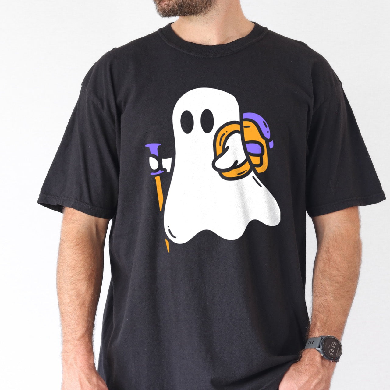Man wearing Black Halloween ghost statement tee with large full front design featuring cute white Boo character holding orange and purple trekking pole with colorful backpack perfect for spooky season celebrations on Comfort Colors shirt for hikers and adventurers. 