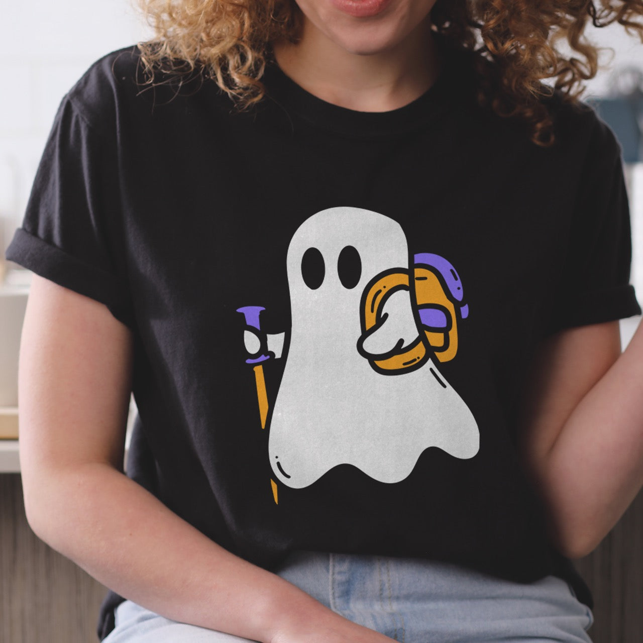 Woman wearing Black Halloween ghost statement tee with large full front design featuring cute white Boo character holding orange and purple trekking pole with colorful backpack perfect for spooky season celebrations on Comfort Colors shirt for hikers and adventurers. 