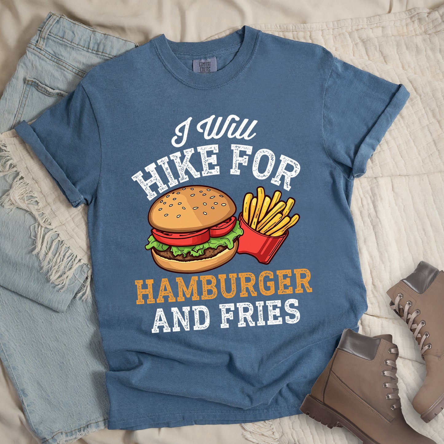 Blue Jean (Denim Blue) t-shirt with white distressed text reading "I Will HIKE FOR HAMBURGER AND FRIES". The words "I Will" appear in white script at the top, "HIKE FOR" in white block letters, "HAMBURGER" in gold/orange, and "AND FRIES" in white at the bottom. Center illustration shows a detailed hamburger with bun, patty, lettuce, and tomato next to a red container of yellow french fries.