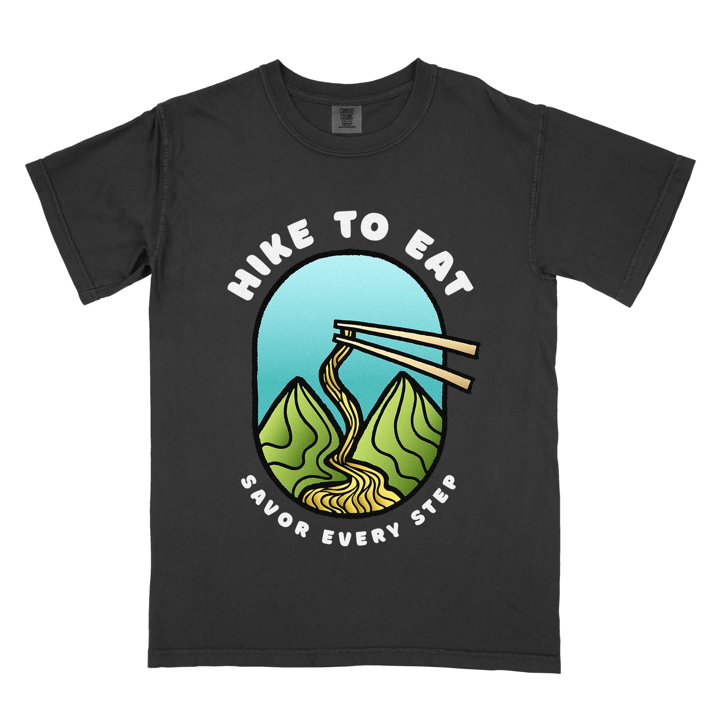 A black t-shirt with white text "HIKE TO EAT" arched at the top and "SAVOR EVERY STEP" at the bottom. The center features an oval graphic with a turquoise blue sky background, green mountain peaks, and chopsticks lifting ramen noodles that flow like a trail between the mountains. 