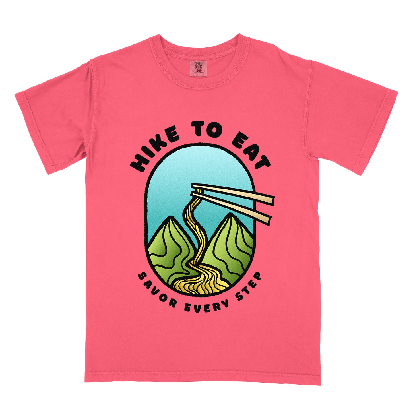 A watermelon (light coral) t-shirt with black text "HIKE TO EAT" arched at the top and "SAVOR EVERY STEP" at the bottom. The center features an oval graphic with a turquoise blue sky background, green mountain peaks, and chopsticks lifting ramen noodles that flow like a trail between the mountains. 
