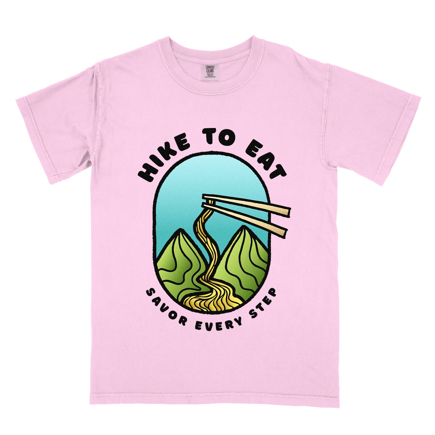 A blossom(light pink) t-shirt with black text "HIKE TO EAT" arched at the top and "SAVOR EVERY STEP" at the bottom. The center features an oval graphic with a turquoise blue sky background, green mountain peaks, and chopsticks lifting ramen noodles that flow like a trail between the mountains. 