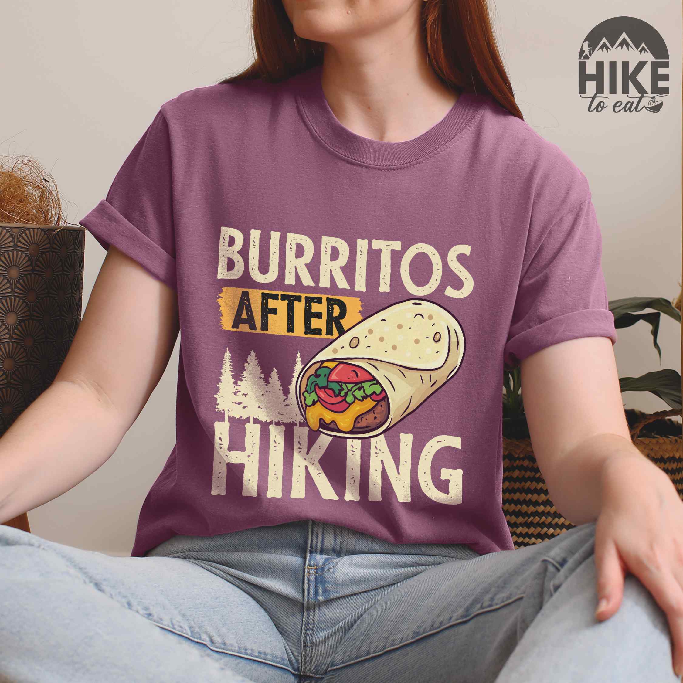woman wearing berry "burritos after hiking" colored vintage tee with bold typography, birds, trees, illustrated wrapped burrito, and backpacker for burrito enthusiasts.