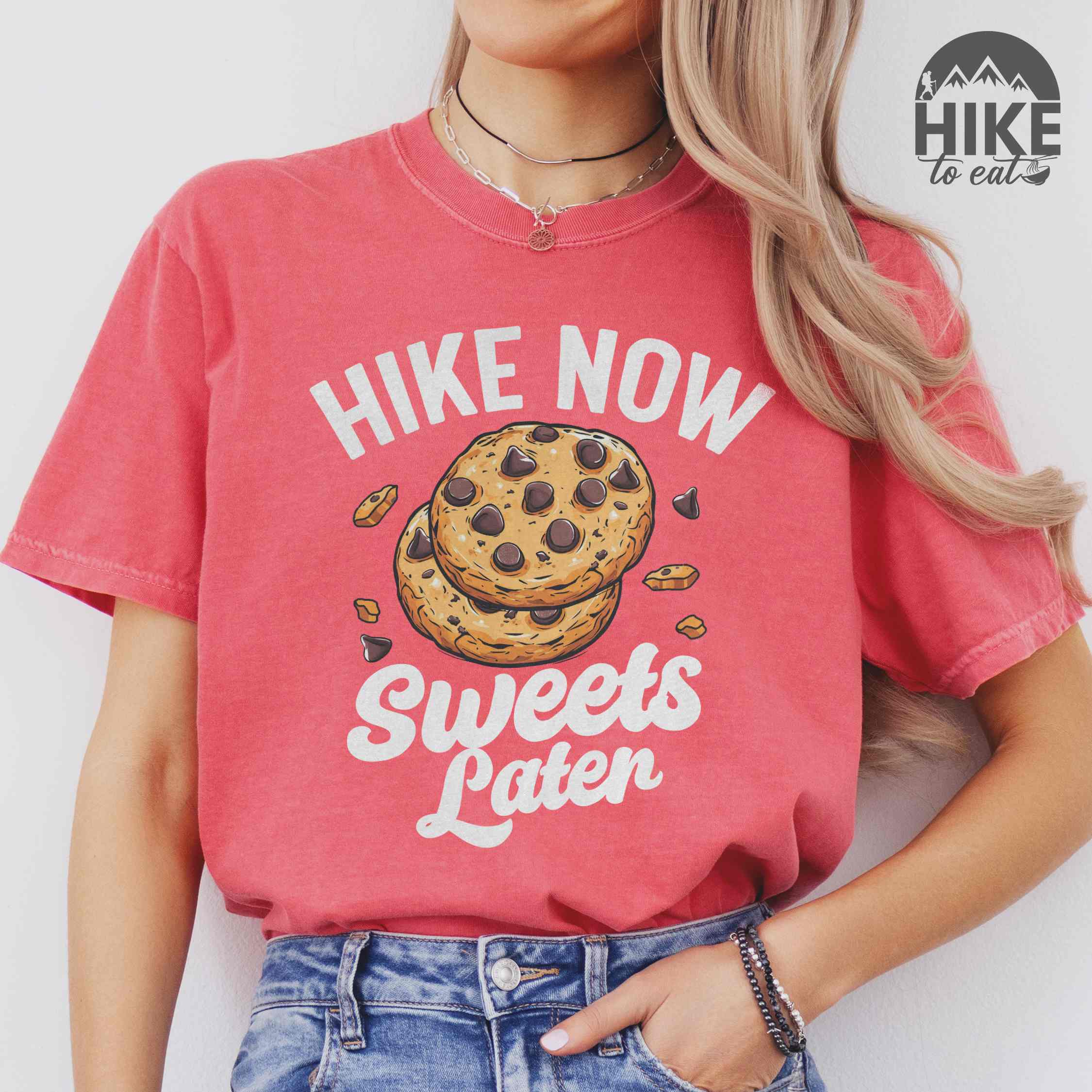 Woman wearing watermelon “Hike Now Sweets Later” colored vintage tee with bold and script typography, illustration of chocolate chip cookies with crumbs scattered around. Perfect for cookie lovers.