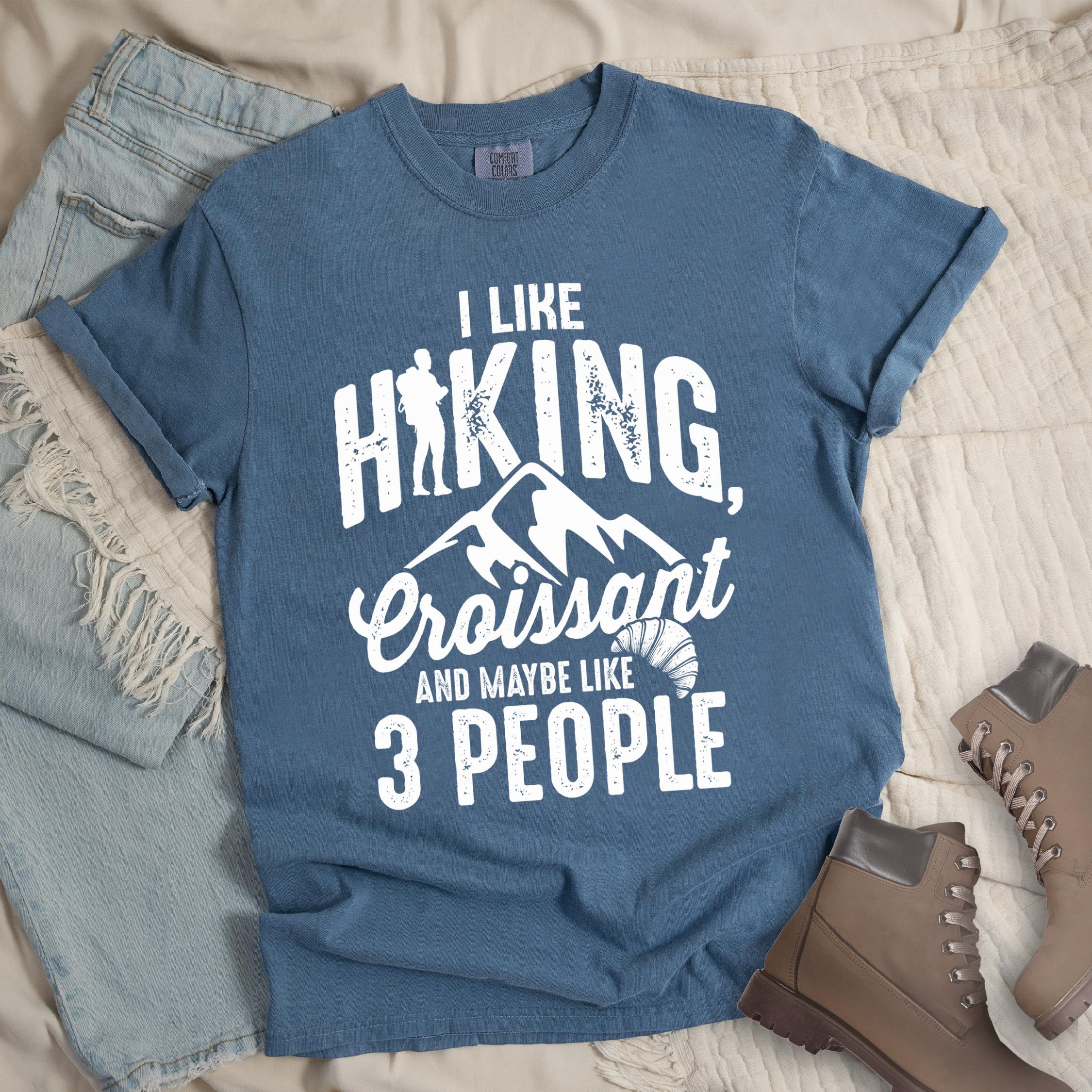 Dark blue shirt with Hiking Design featuring the phrase “I Like Hiking, Croissant, and Maybe Like 3 People” and an illustration of a croissant below mountain outlines.