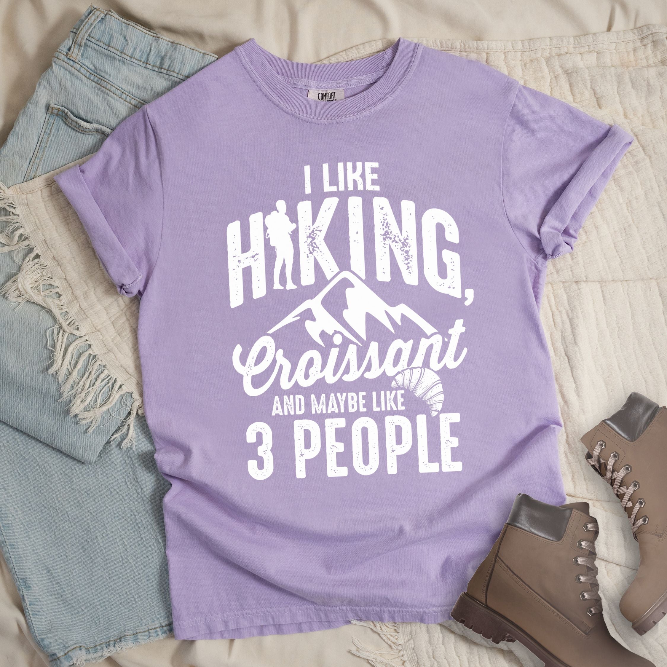 Light purple shirt with Hiking Design featuring the phrase “I Like Hiking, Croissant, and Maybe Like 3 People” and an illustration of a croissant below mountain outlines.