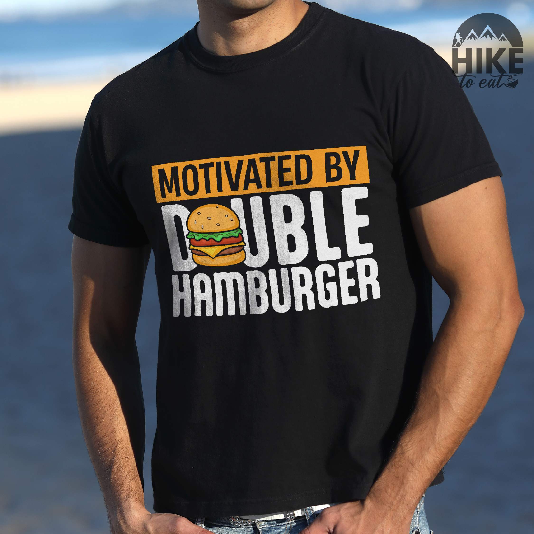 Man wearing black "Motivated by Double Hamburger" colored vintage tee with bold typography, illustrated juicy hamburger, and backpacker for burger enthusiasts.