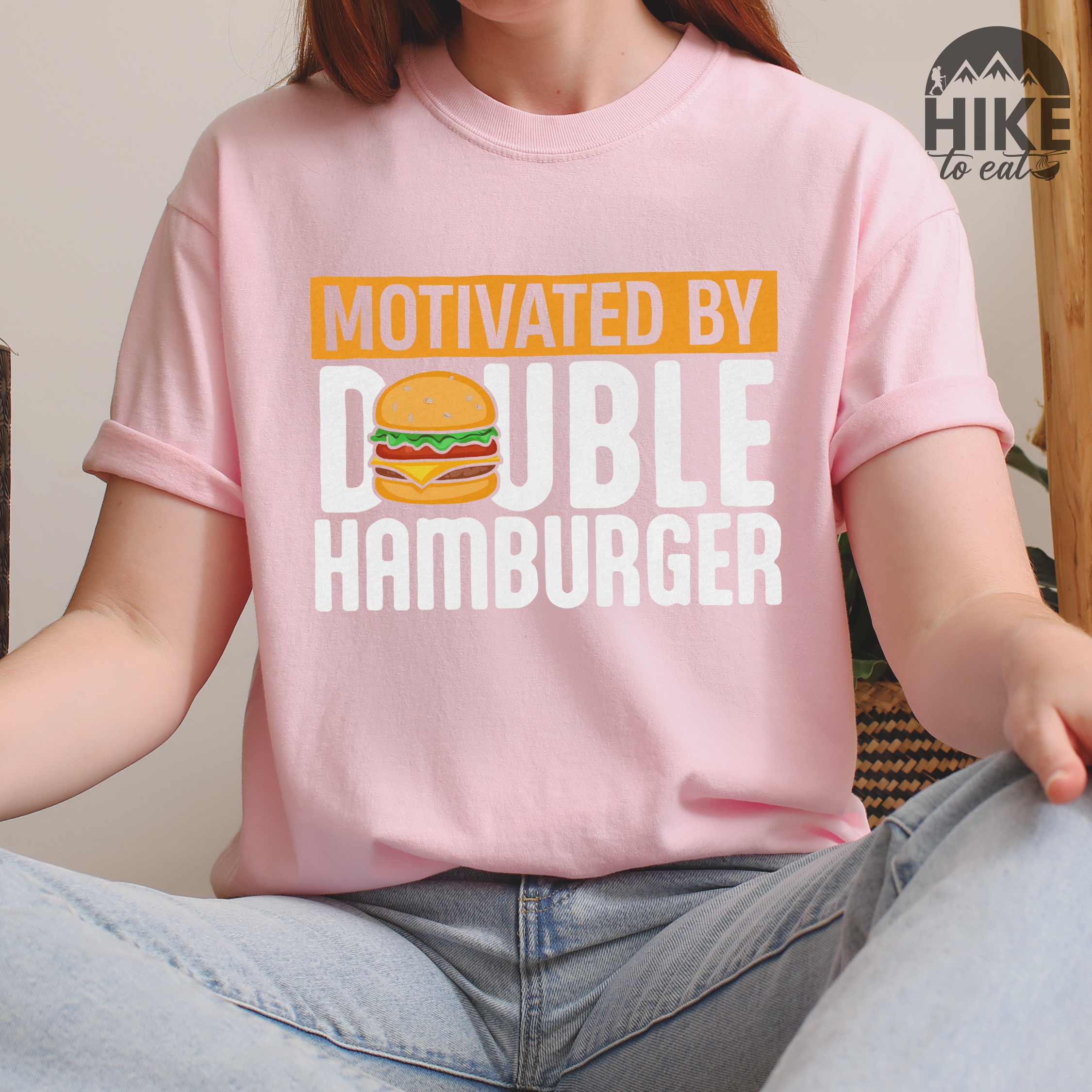 Woman wearing Blossom "Motivated by Double Hamburger" colored vintage tee with bold typography, illustrated juicy hamburger, and backpacker for burger enthusiasts.
