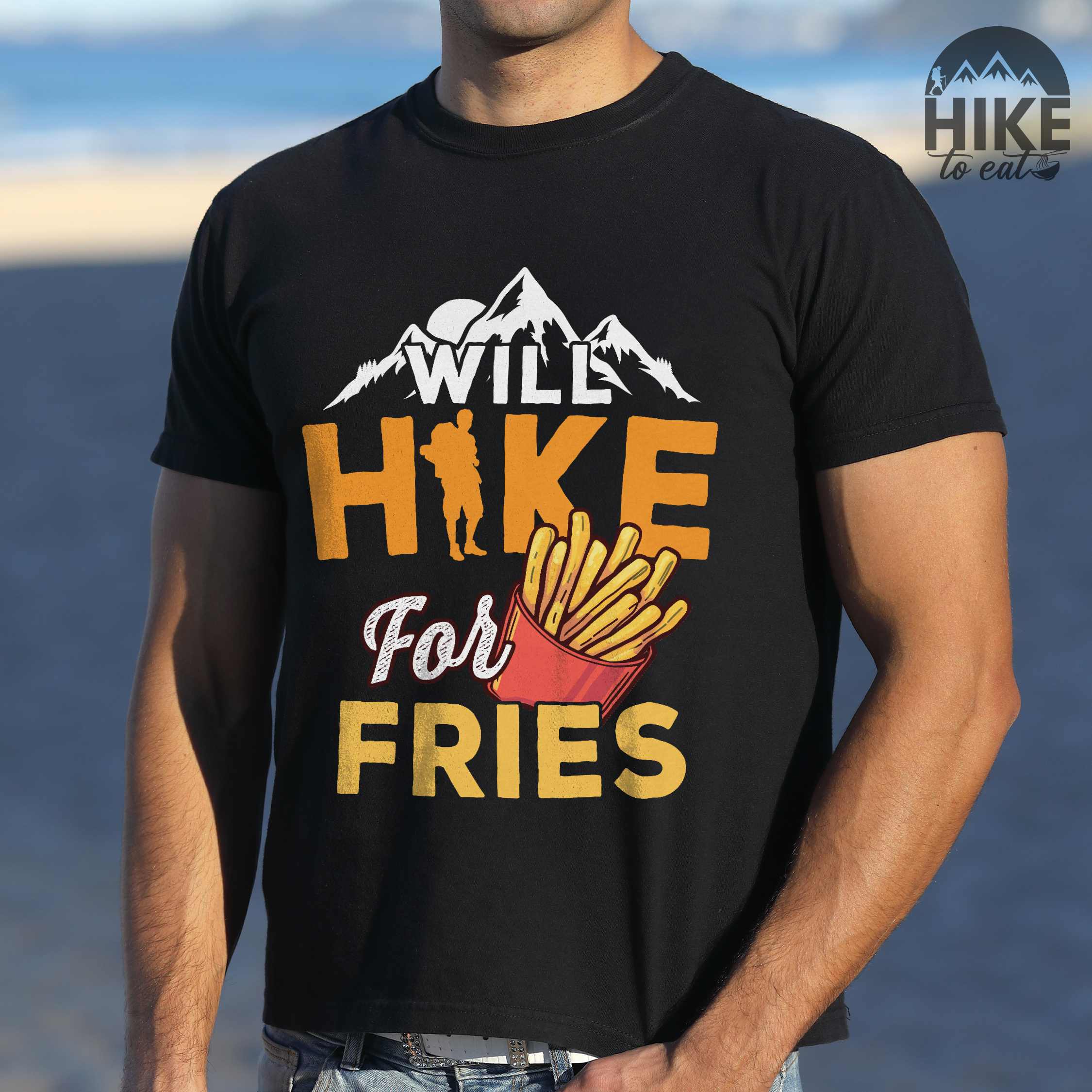 Man wearing black "Will Hike for Fries" colored vintage tee with bold typography, mountains, illustrated fries, and backpacker for comfort food enthusiasts.