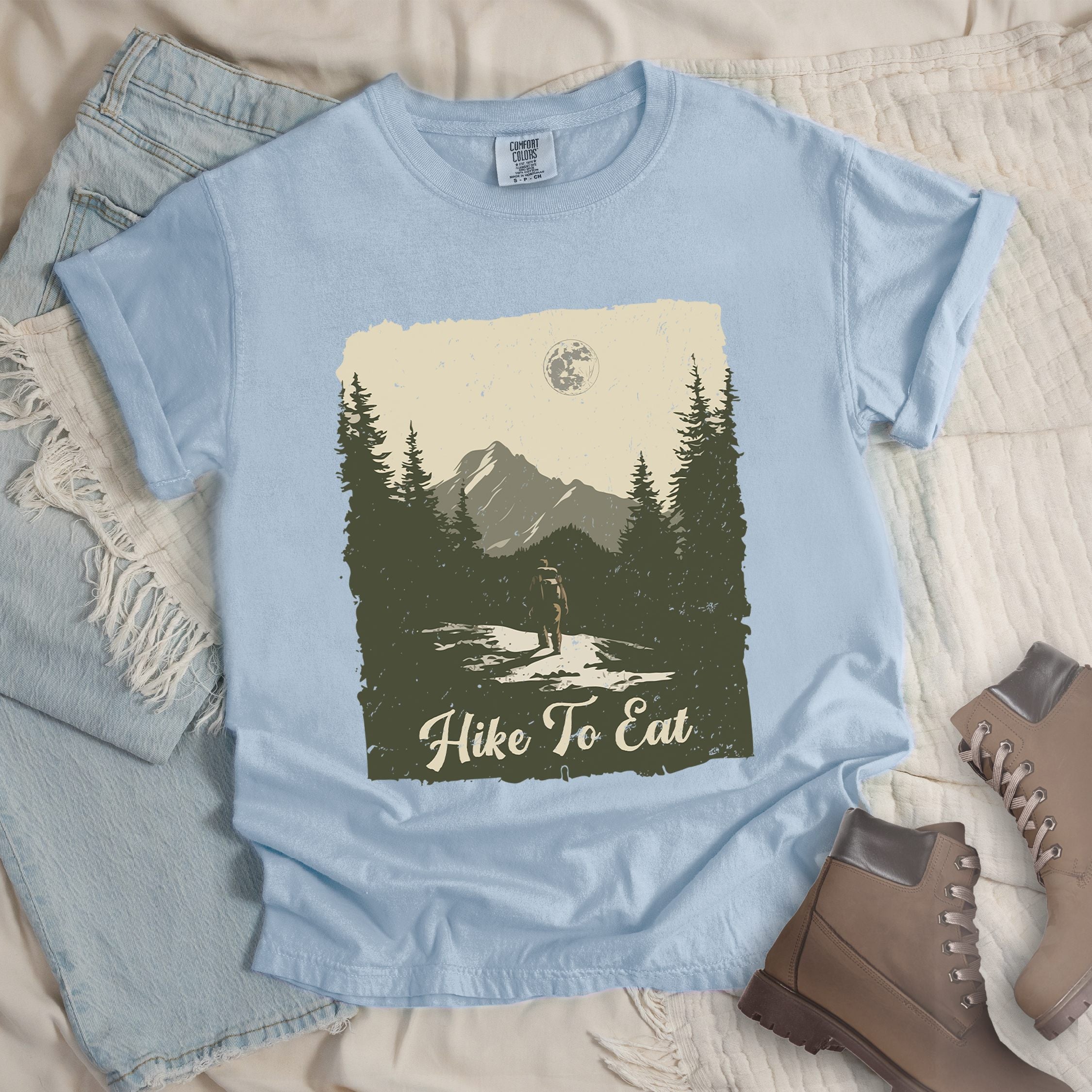 Light blue shirt with Hiking Design featuring the phrase “Hike to Eat” and an illustration of a lone hiker walking toward mountains under the moonlight in a nature scene.