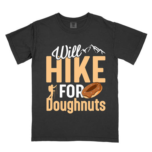 Black t-shirt with "Will HIKE FOR Doughnuts" graphic design. White script "Will" above tan "HIKE" in bold letters, with small mountain peaks above. "FOR" appears in white, followed by "Doughnuts" in tan, with an illustrated chocolate donut replacing the "O" in "FOR". Features a small hiker silhouette. 
