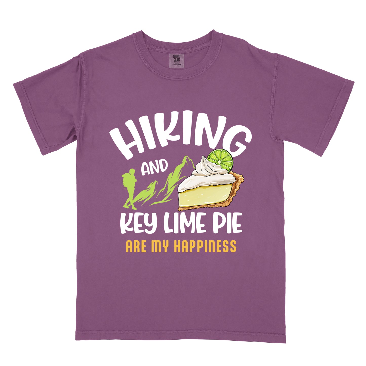 Berry (Dark Violet) t-shirt with text "HIKING AND KEY LIME PIE ARE MY HAPPINESS". "HIKING" appears in white arched letters at the top, "AND" in small white text, "KEY LIME PIE" in large white text in the middle, and "ARE MY HAPPINESS" in gold/yellow at the bottom. The design includes green mountain silhouettes with a hiker silhouette and an illustration of a slice of key lime pie with whipped cream and lime garnish in between "AND" and "KEY LIME PIE." 