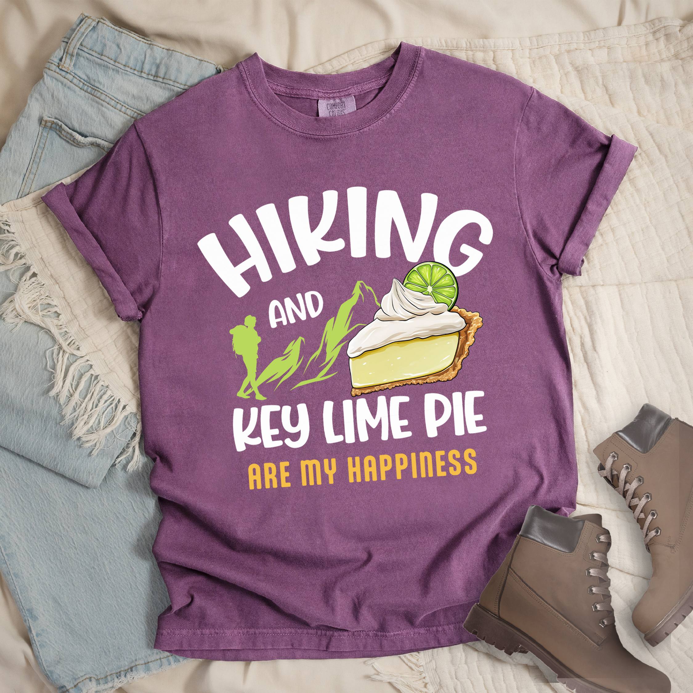 Dark pink shirt with Hiking Design featuring the phrase “Hiking and Key Lime Pie Are My Happiness” and an illustration of a key lime pie slice topped with whipped cream and a lime slice beside green mountain graphics.