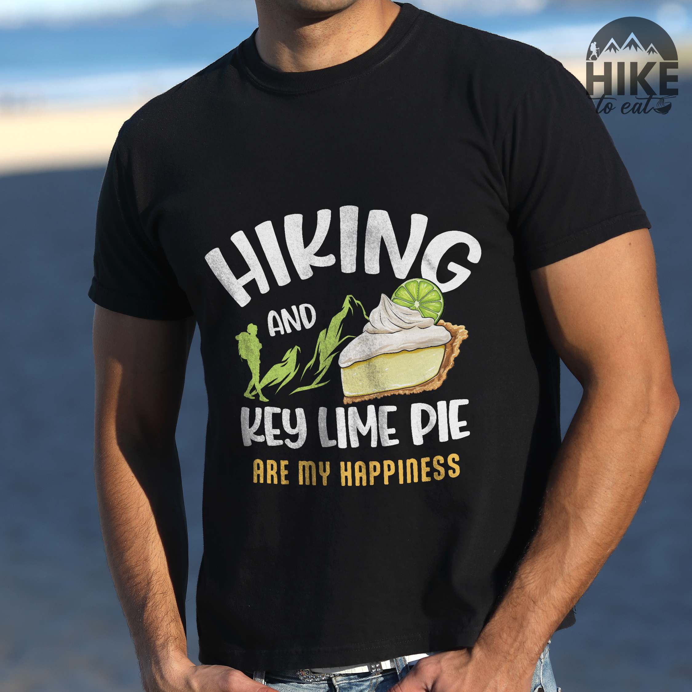 Man wearing black "Hiking and key lime pie are my happiness" colored vintage tee with bold typography, mountains, birds, illustrated slice of key lime pie, and backpacker for pie lovers.
