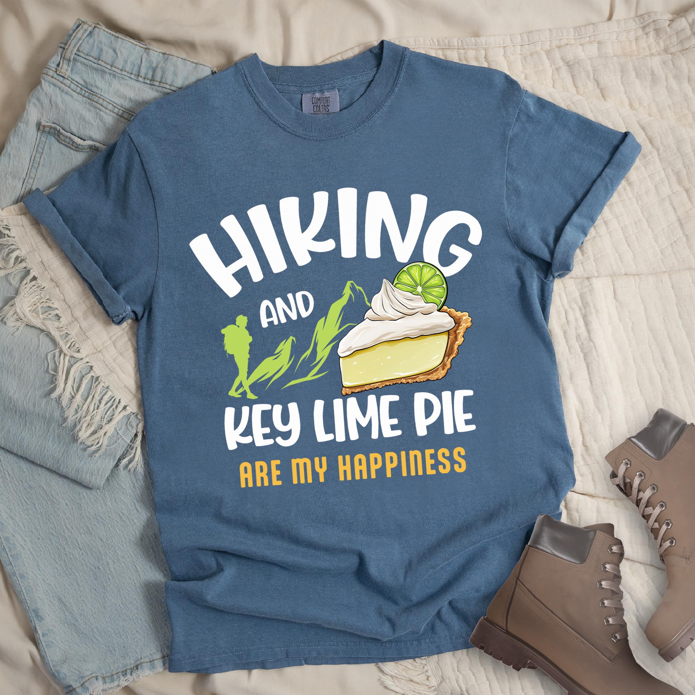 Dark blue shirt with Hiking Design featuring the phrase “Hiking and Key Lime Pie Are My Happiness” and an illustration of a key lime pie slice topped with whipped cream and a lime slice beside green mountain graphics.