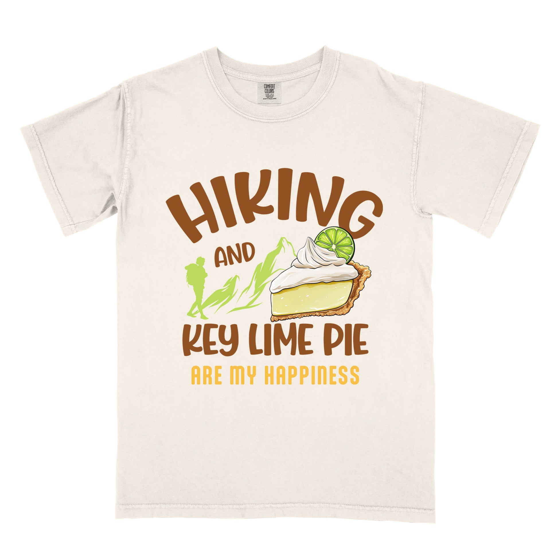 Ivory (Cream White) t-shirt with text "HIKING AND KEY LIME PIE ARE MY HAPPINESS". "HIKING" appears in brown arched letters at the top, "AND" in small brown text, "KEY LIME PIE" in large brown text in the middle, and "ARE MY HAPPINESS" in gold/yellow at the bottom. The design includes green mountain silhouettes with a hiker silhouette and an illustration of a slice of key lime pie with whipped cream and lime garnish in between "AND" and "KEY LIME PIE." 