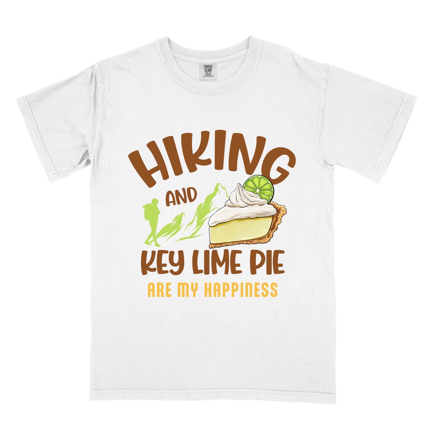 White t-shirt with text "HIKING AND KEY LIME PIE ARE MY HAPPINESS". "HIKING" appears in brown arched letters at the top, "AND" in small brown text, "KEY LIME PIE" in large brown text in the middle, and "ARE MY HAPPINESS" in gold/yellow at the bottom. The design includes green mountain silhouettes with a hiker silhouette and an illustration of a slice of key lime pie with whipped cream and lime garnish in between "AND" and "KEY LIME PIE." 