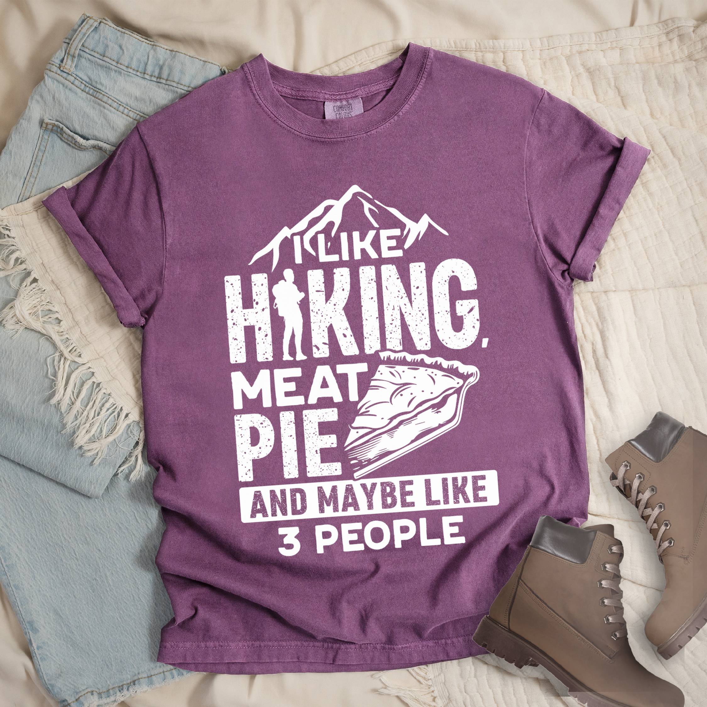 Dark pink shirt with Hiking Design featuring the phrase “I Like Hiking, Meat Pie, and Maybe Like 3 People” with a hiker silhouette, mountain outline, and an illustration of a meat pie slice.