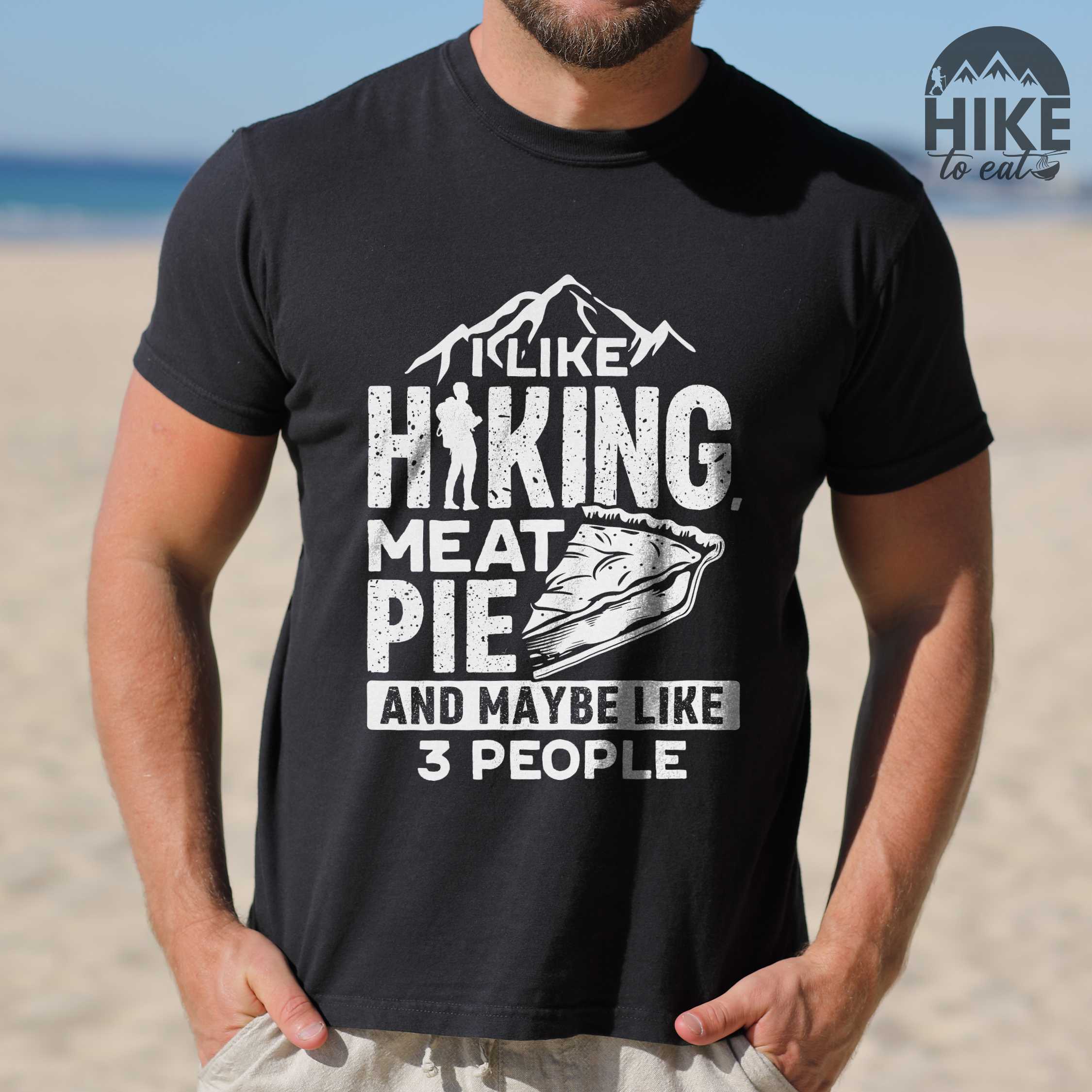 Man wearing black "I like hiking, meat pie and maybe like 3 people" colored vintage tee with bold typography, mountains, birds, illustrated slice of meat pie, and backpacker for pie lovers.
